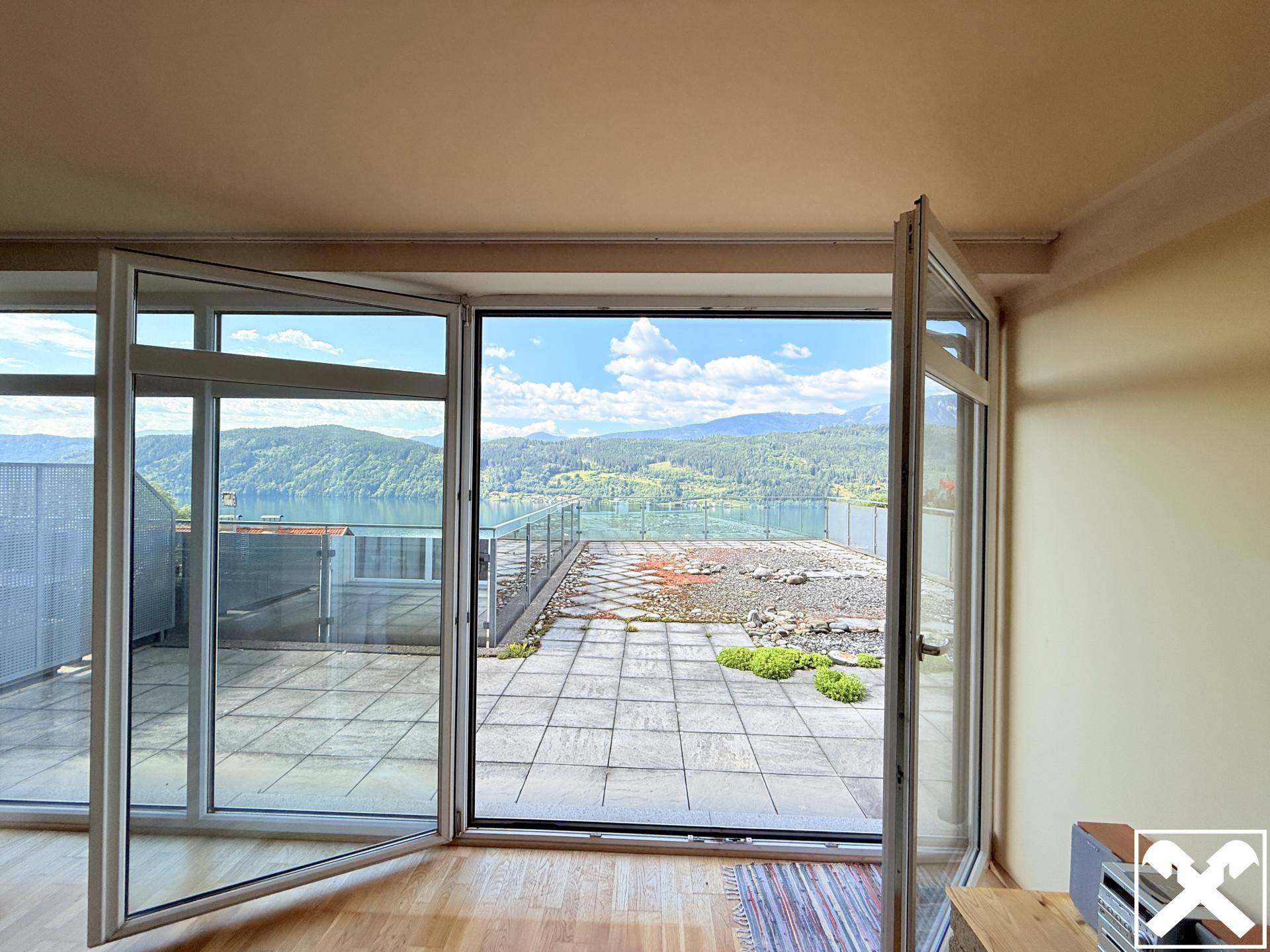 Lichtdurchfluteter Raum mit großen Fenstertüren, die auf eine Terrasse mit Panoramablick auf den See und die Berge führen.