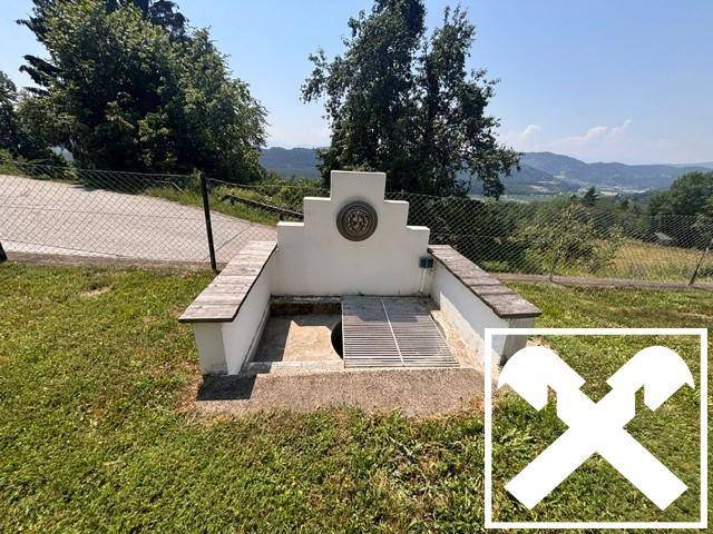 Dekorativer Brunnen oder Wasserstelle im Garten mit weitem Blick ins Grüne.