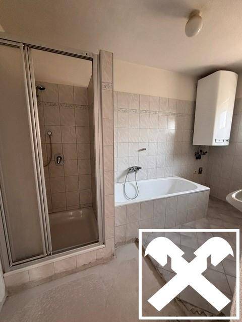 Badezimmer mit Badewanne, Duschkabine und gefliesten Wänden, teilweise renovierungsbedürftig.