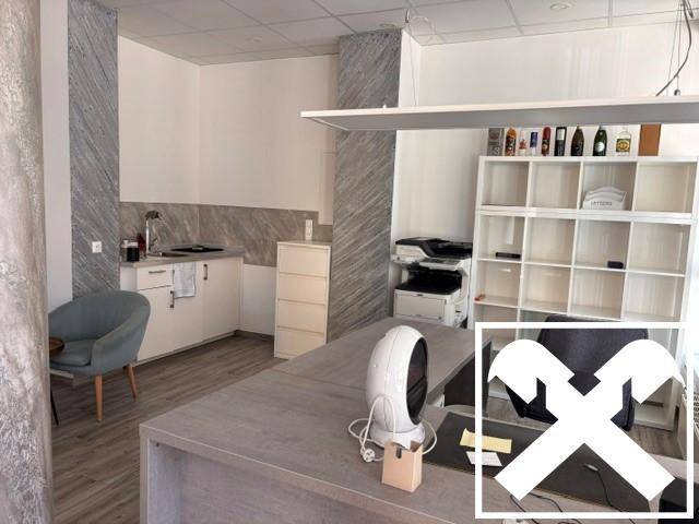 Modernes Büro mit kleiner Küchenzeile, Schreibtisch und Regalen für Arbeitsmaterialien.