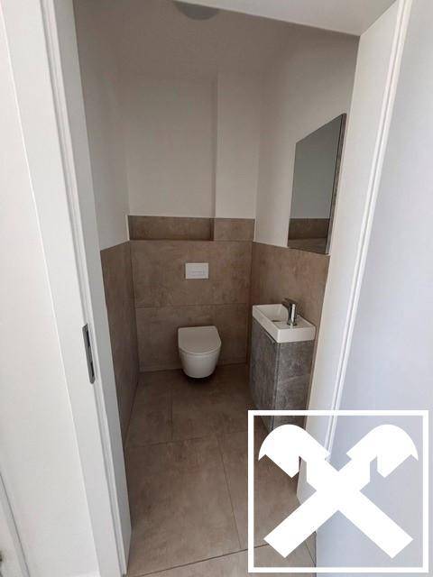 Modernes Gäste-WC mit wandhängender Toilette und kleinem Waschbecken, halbhoch gefliest.