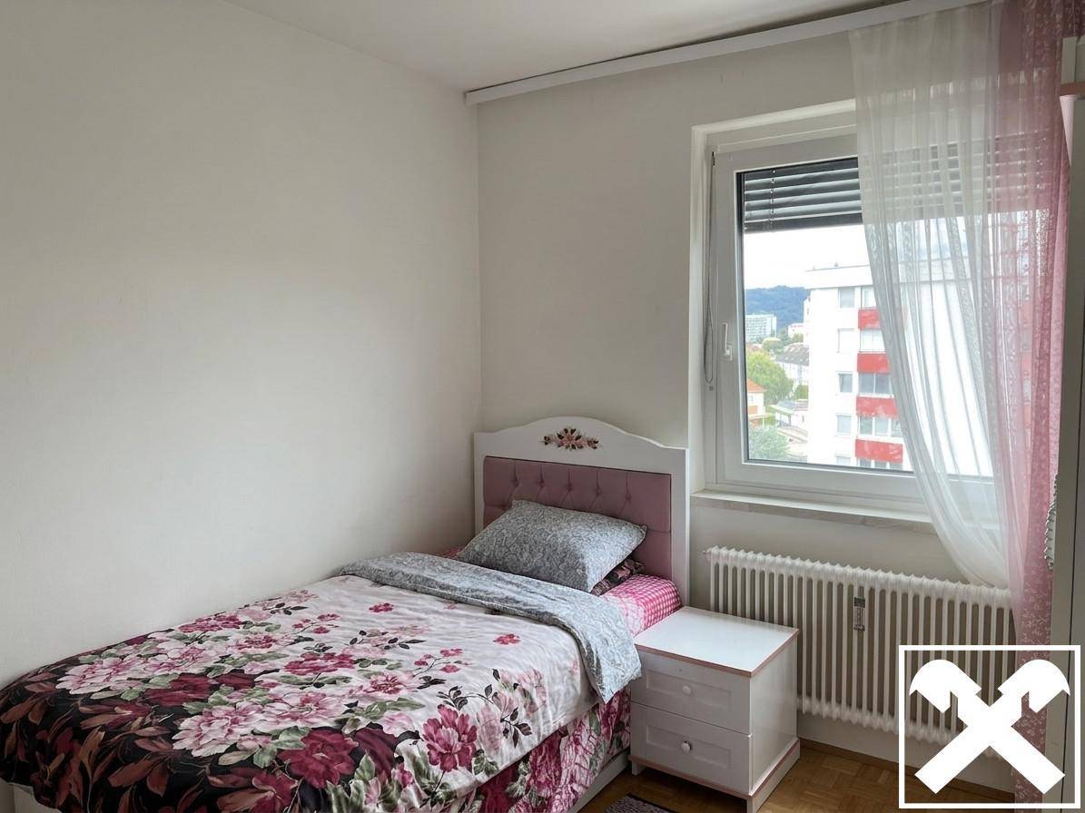 Kinderzimmer mit Einzelbett, floraler Bettwäsche, Nachttisch und Blick auf die umliegenden Gebäude.