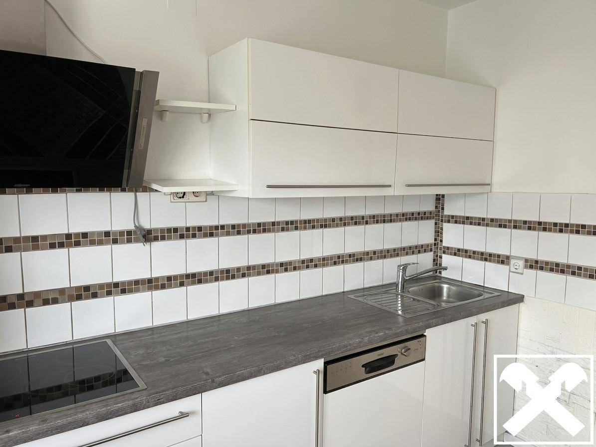 Moderne Küche mit weißen Schränken, grauer Arbeitsplatte, Induktionskochfeld und integriertem Geschirrspüler.