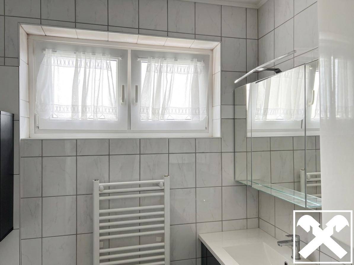 Helles Badezimmer mit Fenster, beheiztem Handtuchhalter, Waschtisch und Spiegelschrank.