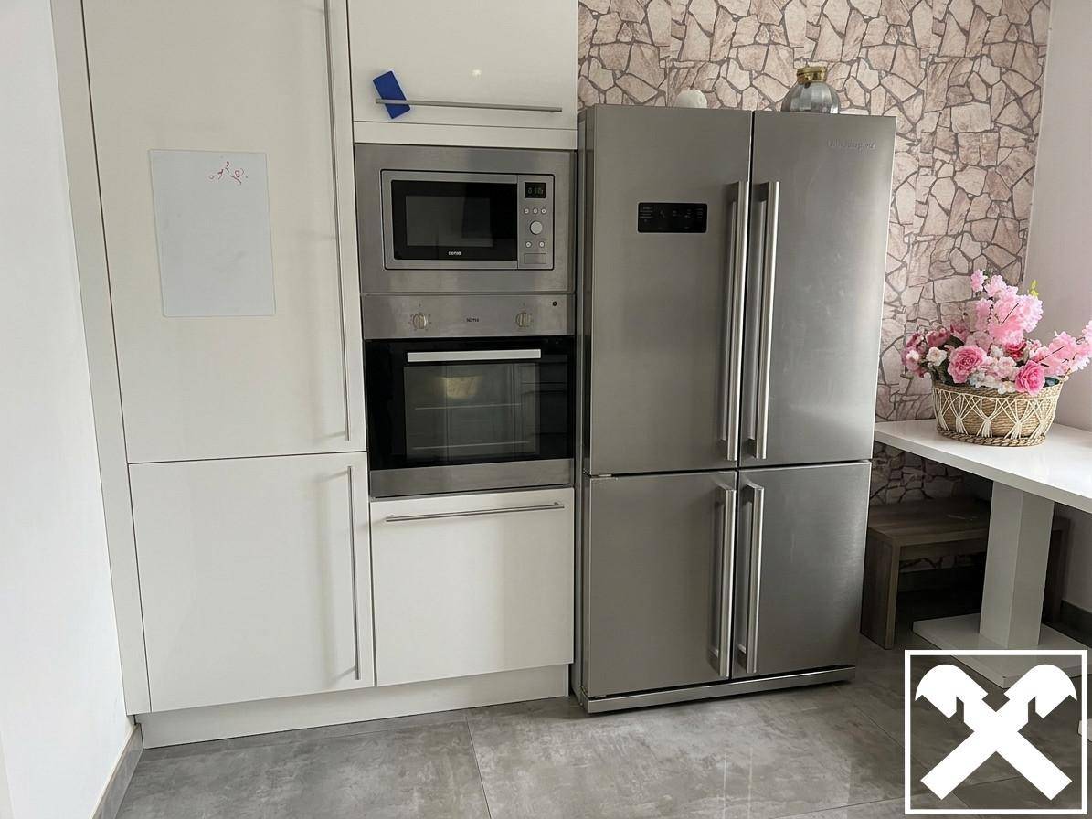 Küchenzeile mit integriertem Backofen, Mikrowelle und großem Edelstahlkühlschrank neben gemusterter Tapete.