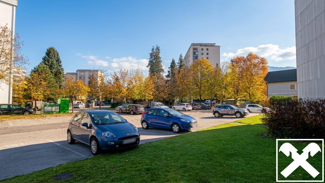 Außenparkplatz mit mehreren Autos, Bäumen in Herbstfarben und Wohngebäuden im Hintergrund.