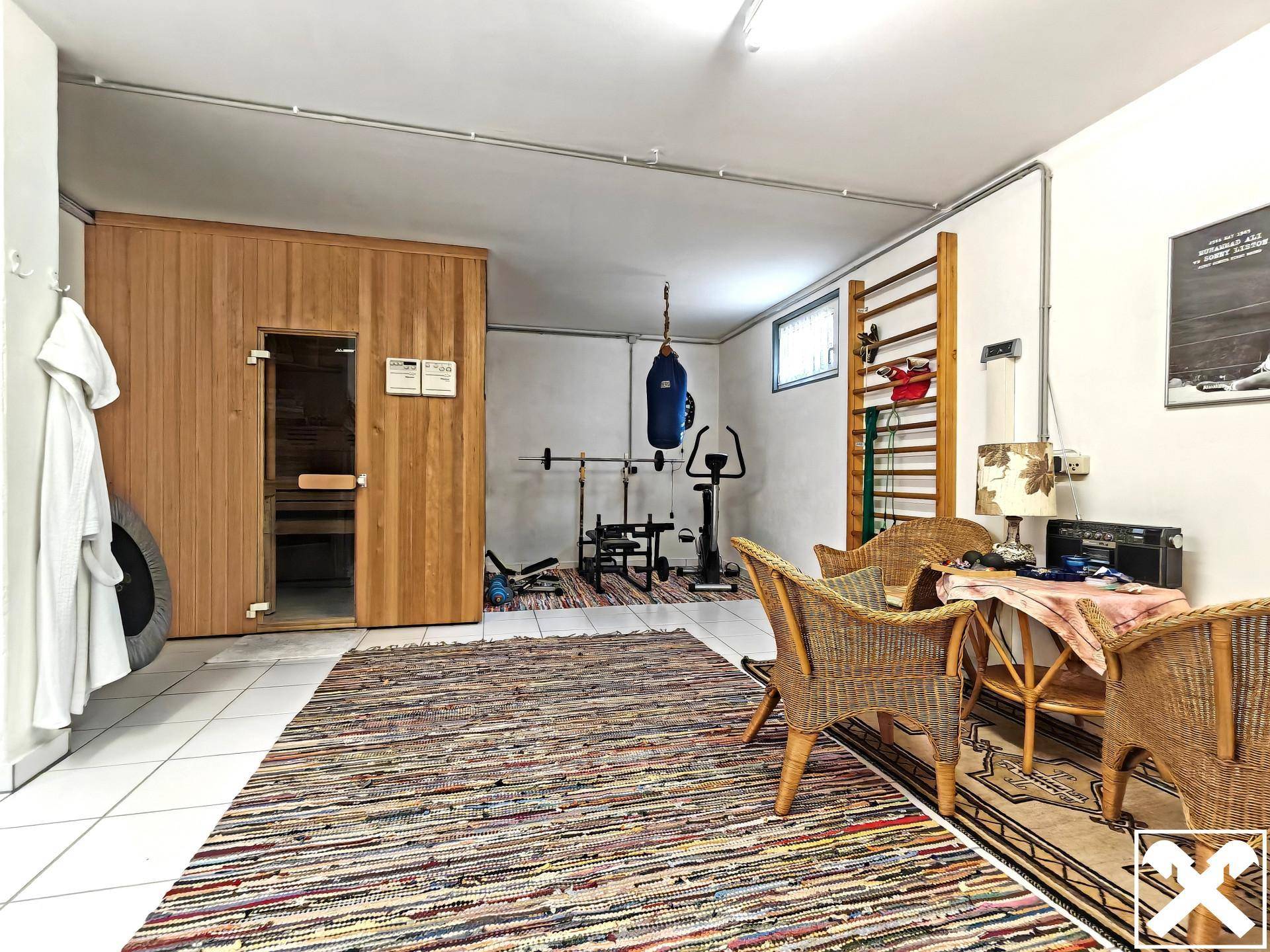 Fitnessraum im Keller mit Sauna, Sportgeräten und Sitzgelegenheiten.