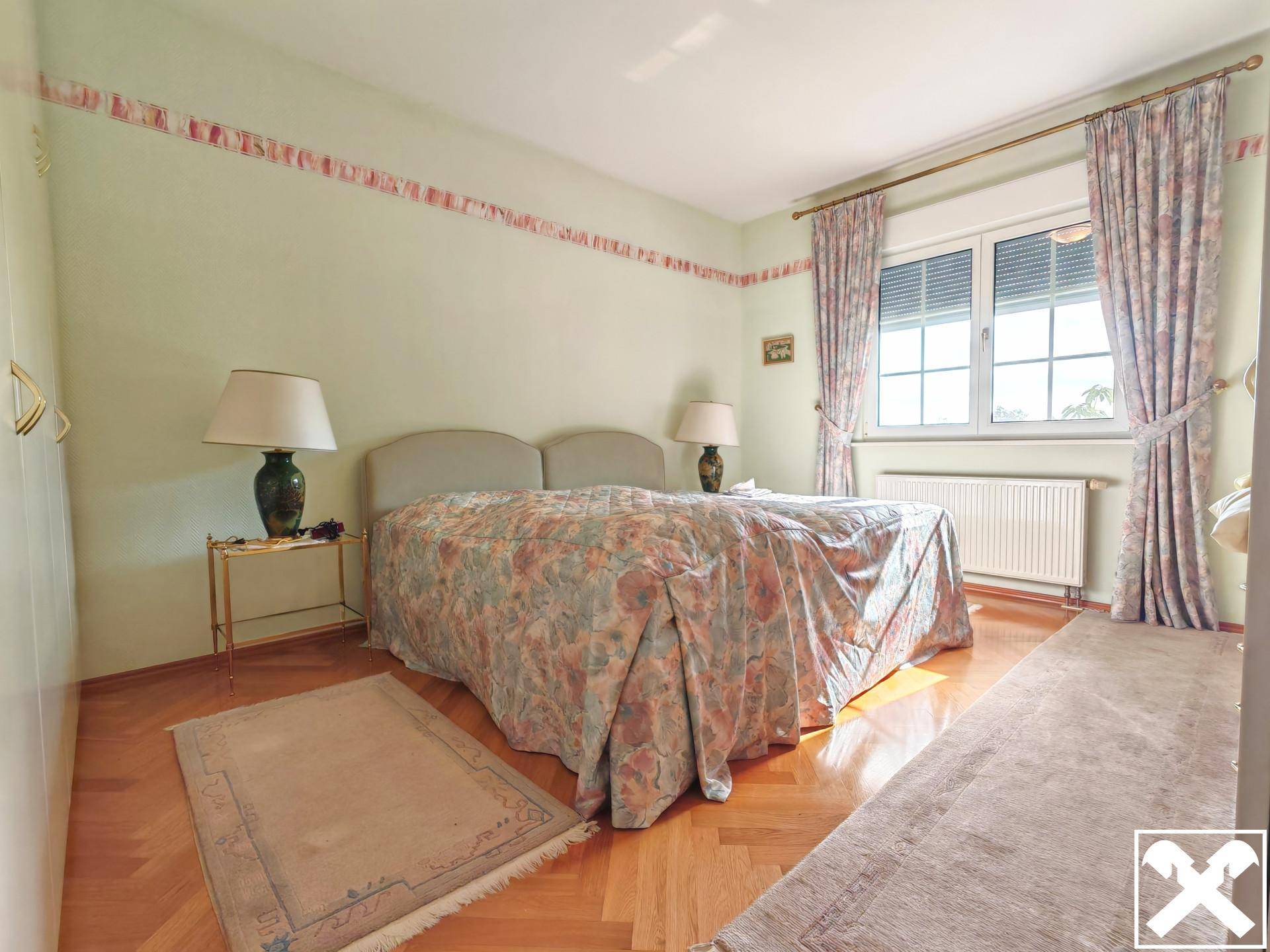Schlafzimmer mit Parkettboden, Doppelbett und Fenster mit Rollläden.