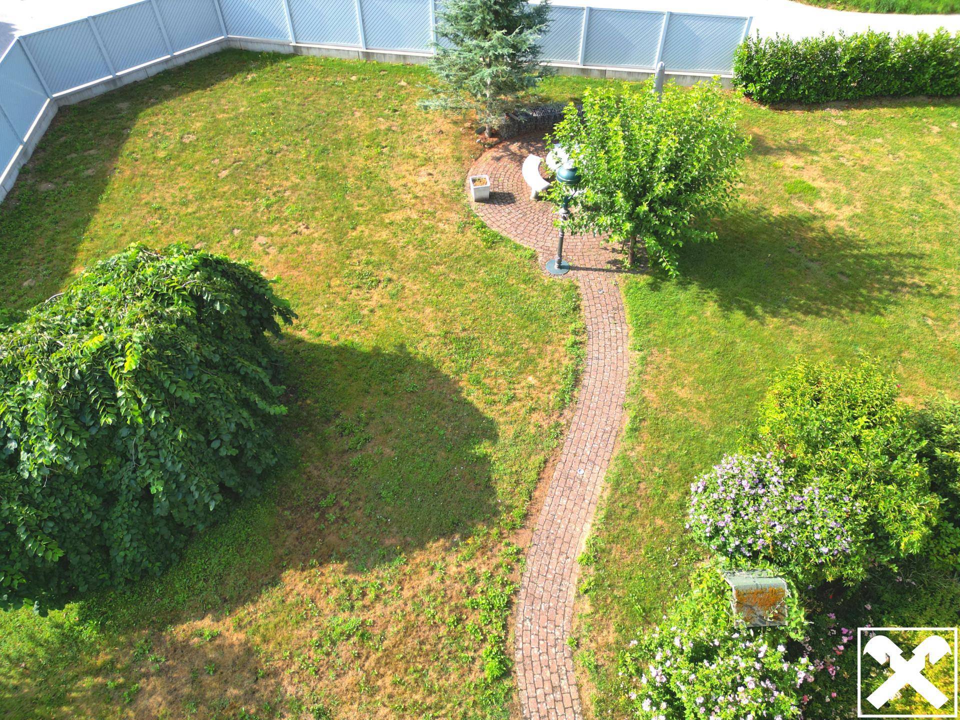 Gartenbereich mit einem gepflasterten Weg, Rasenflächen und verschiedenen Sträuchern.