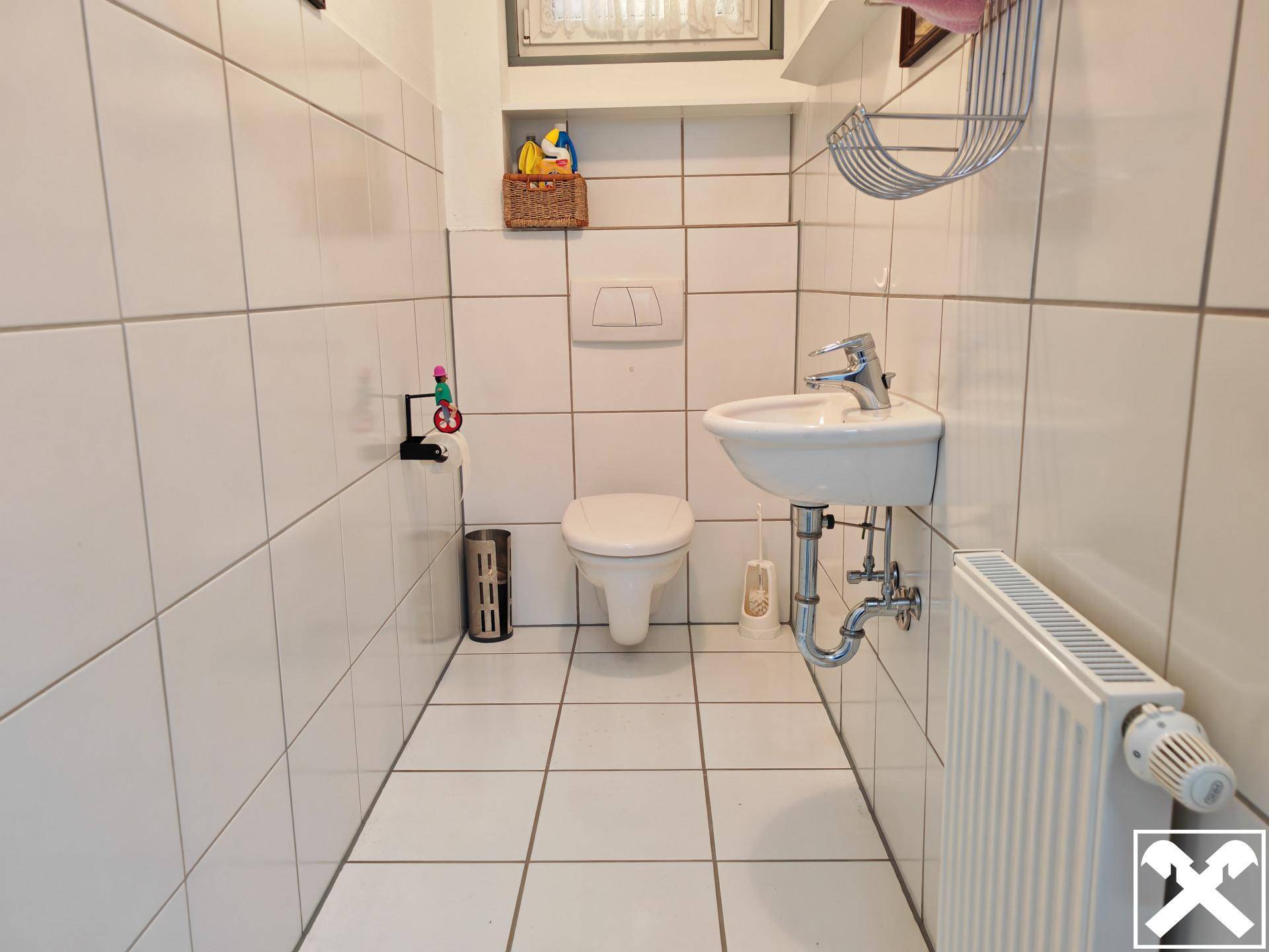 Kleines WC mit weißen Fliesen, Wand-WC und Waschbecken.