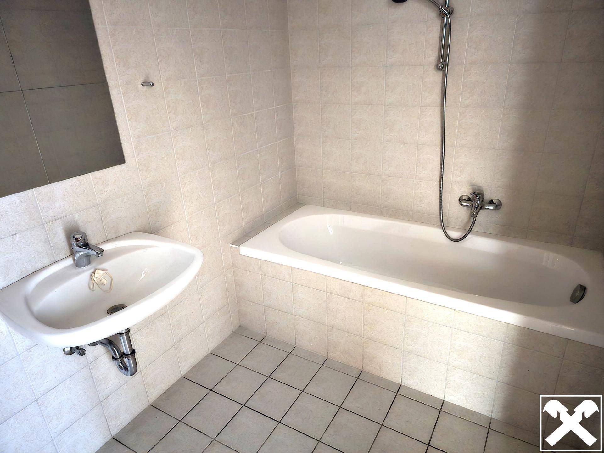 Badezimmer mit Badewanne, Waschbecken und hellen Fliesen an Wänden und Boden.