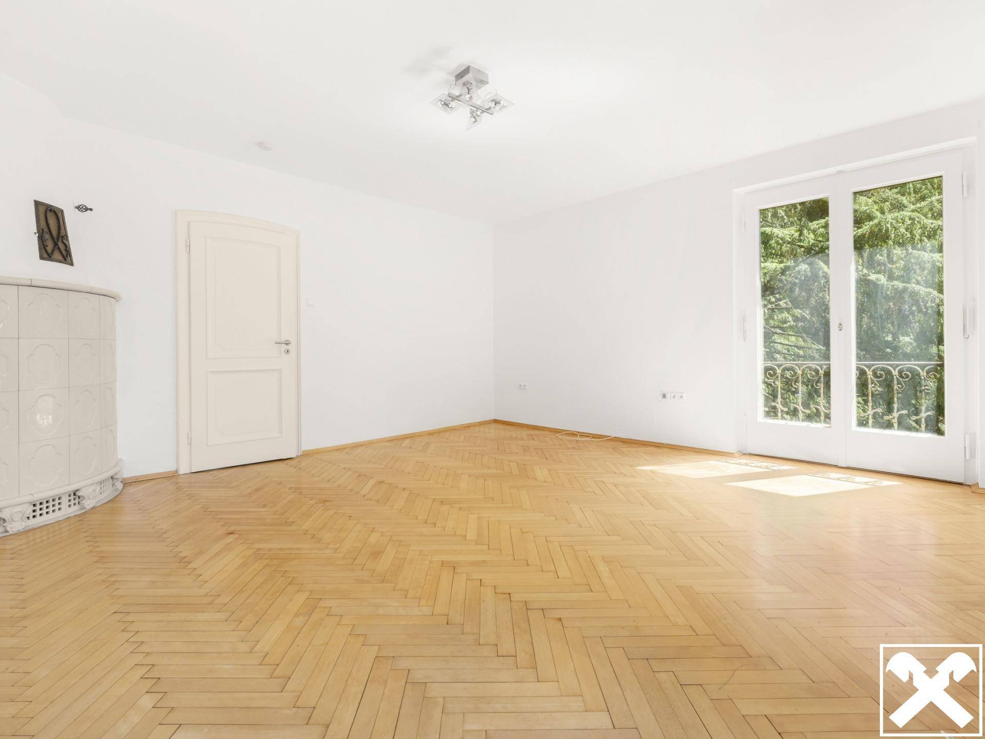 Geräumiges Zimmer mit Fischgrätparkett, Kachelofen und Zugang zu einem französischen Balkon.