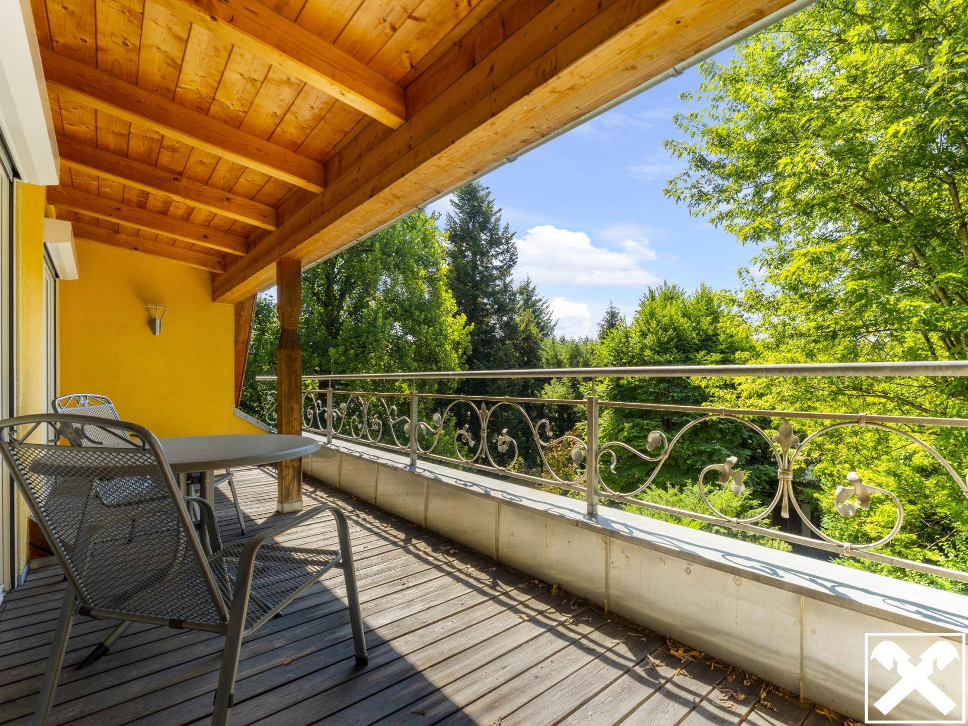 Geräumiger Balkon mit Holzboden, Sitzgelegenheiten und einem schönen Blick ins Grüne.