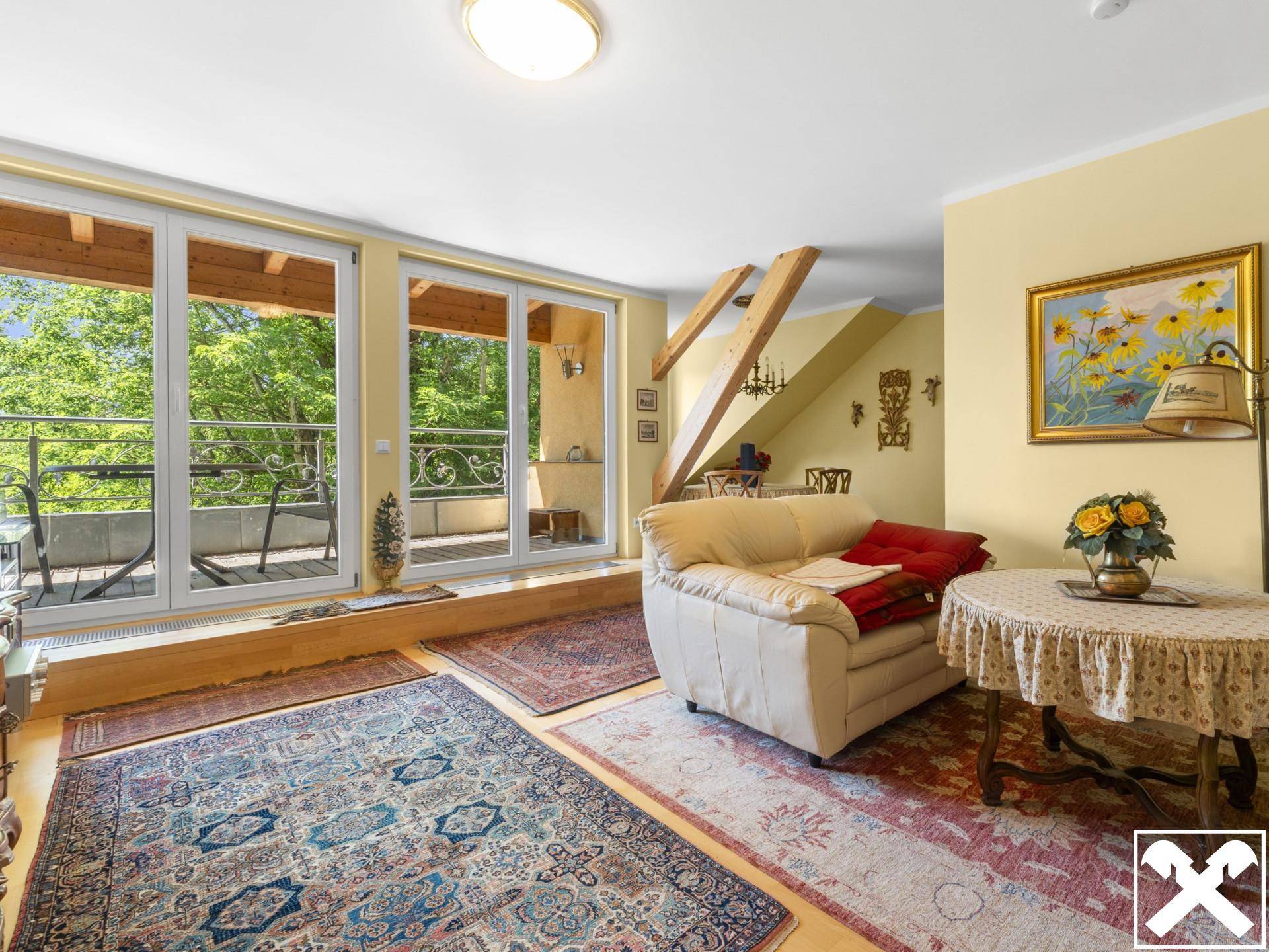 Gemütliches Wohnzimmer mit Zugang zum Balkon, Holzbalken und schrägen Decken, dekoriert mit Teppichen.