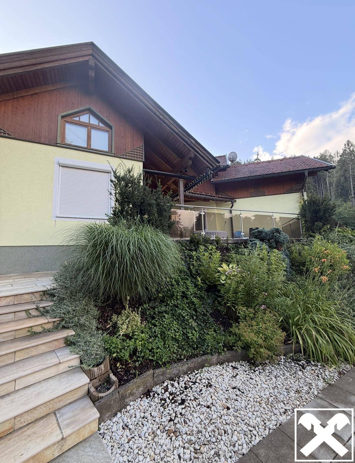Terrasse mit Glasgeländer und üppiger Bepflanzung vor dem Haupthaus.
