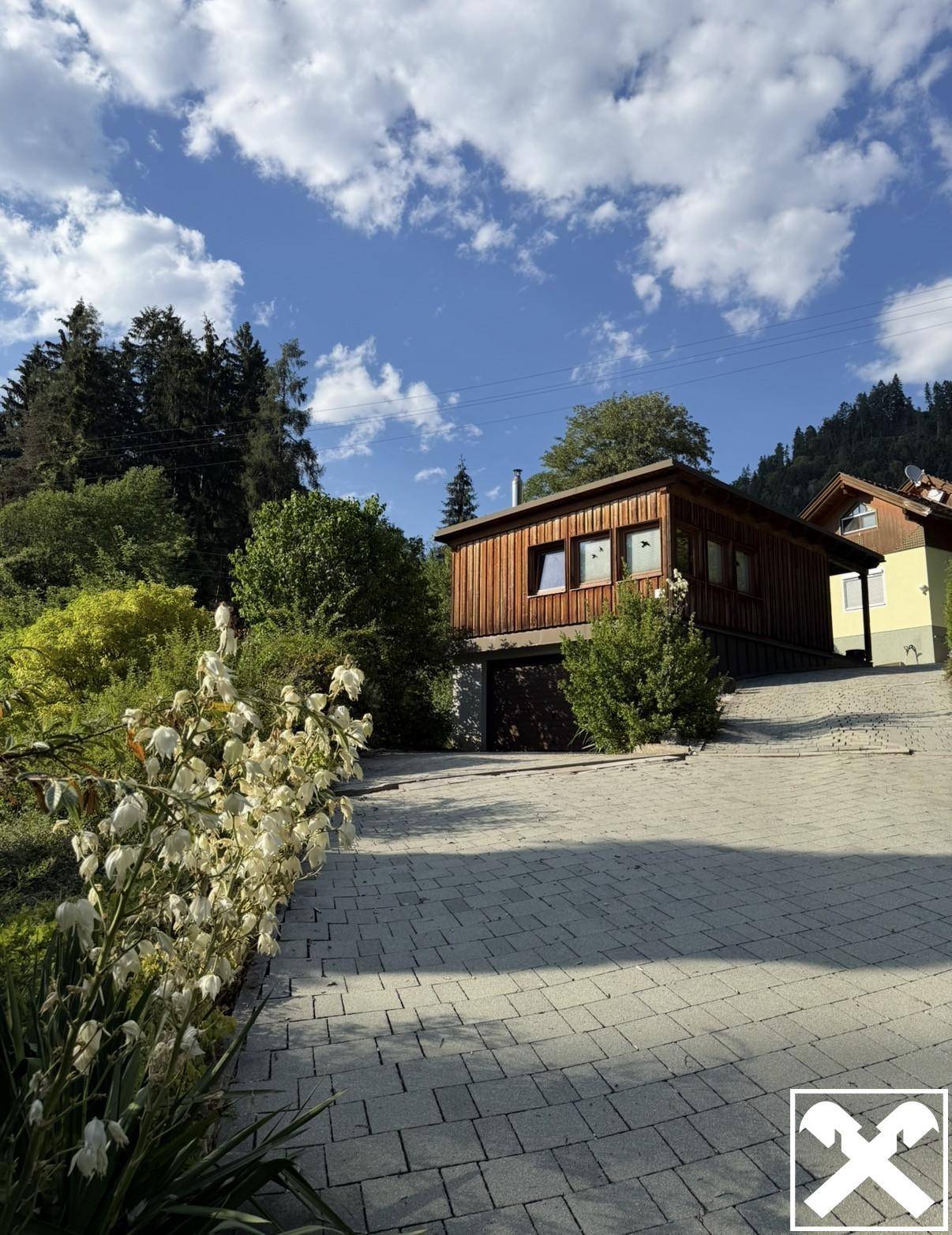 Gepflasterte Auffahrt führt zu einem Nebengebäude mit Holzfassade und Garagentor.