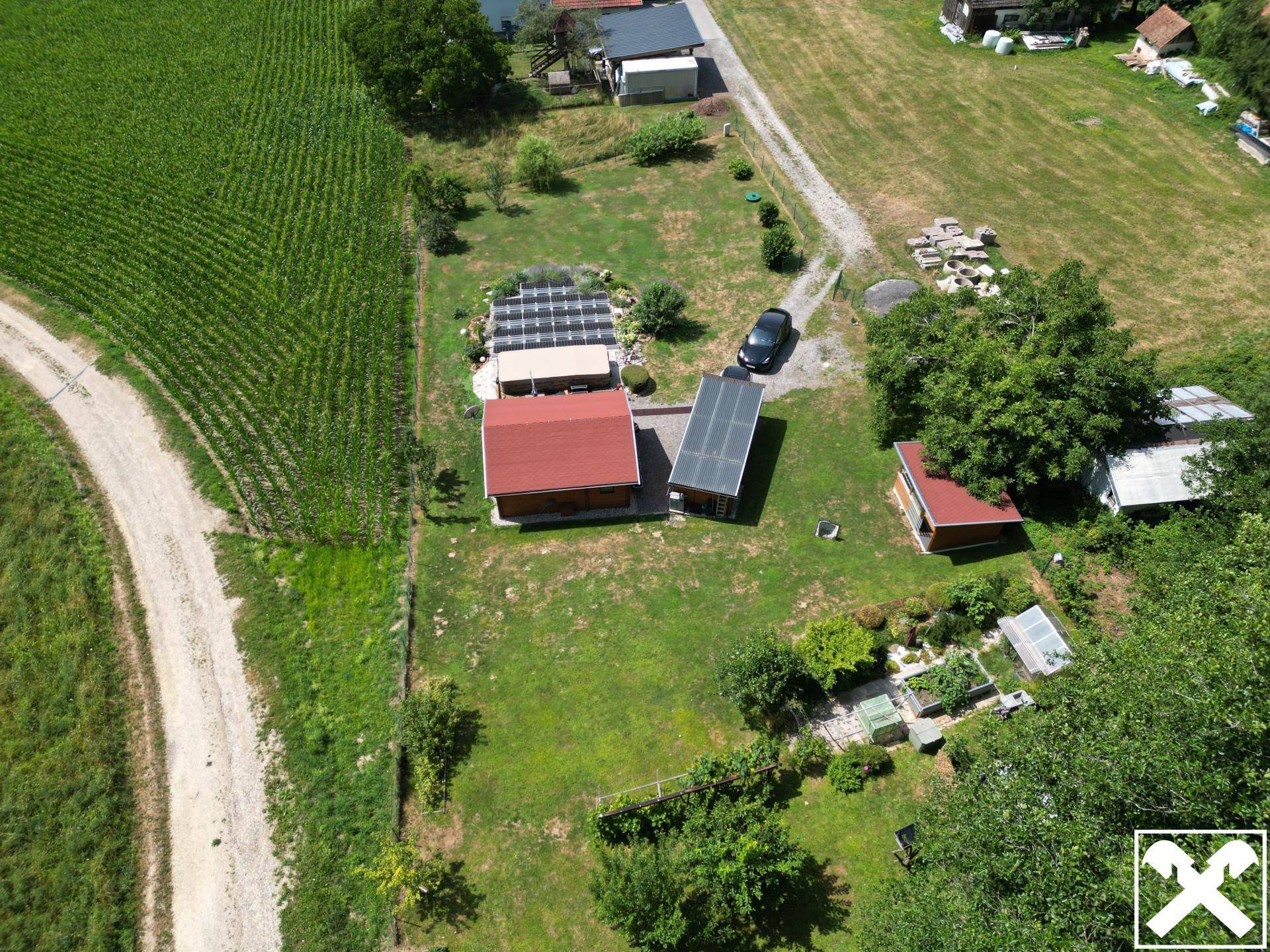 Weitläufige Luftaufnahme des Grundstücks mit Holzhaus, Solaranlage, Garten und angrenzenden Feldern und Wegen.