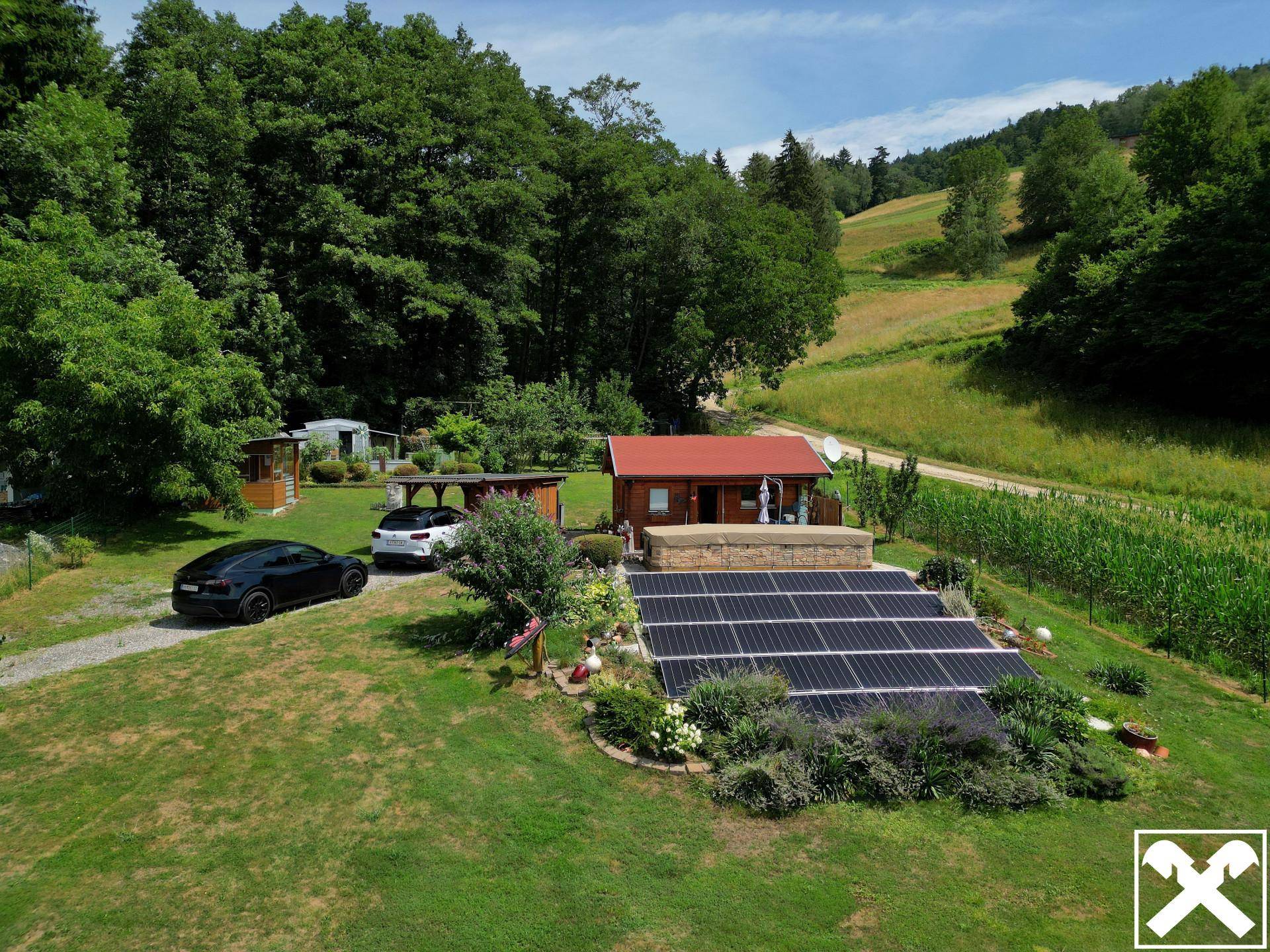 Luftaufnahme des Anwesens mit Holzhaus, Solaranlage, Whirlpool und weitläufiger Grünfläche umgeben von Wald und Feldern.