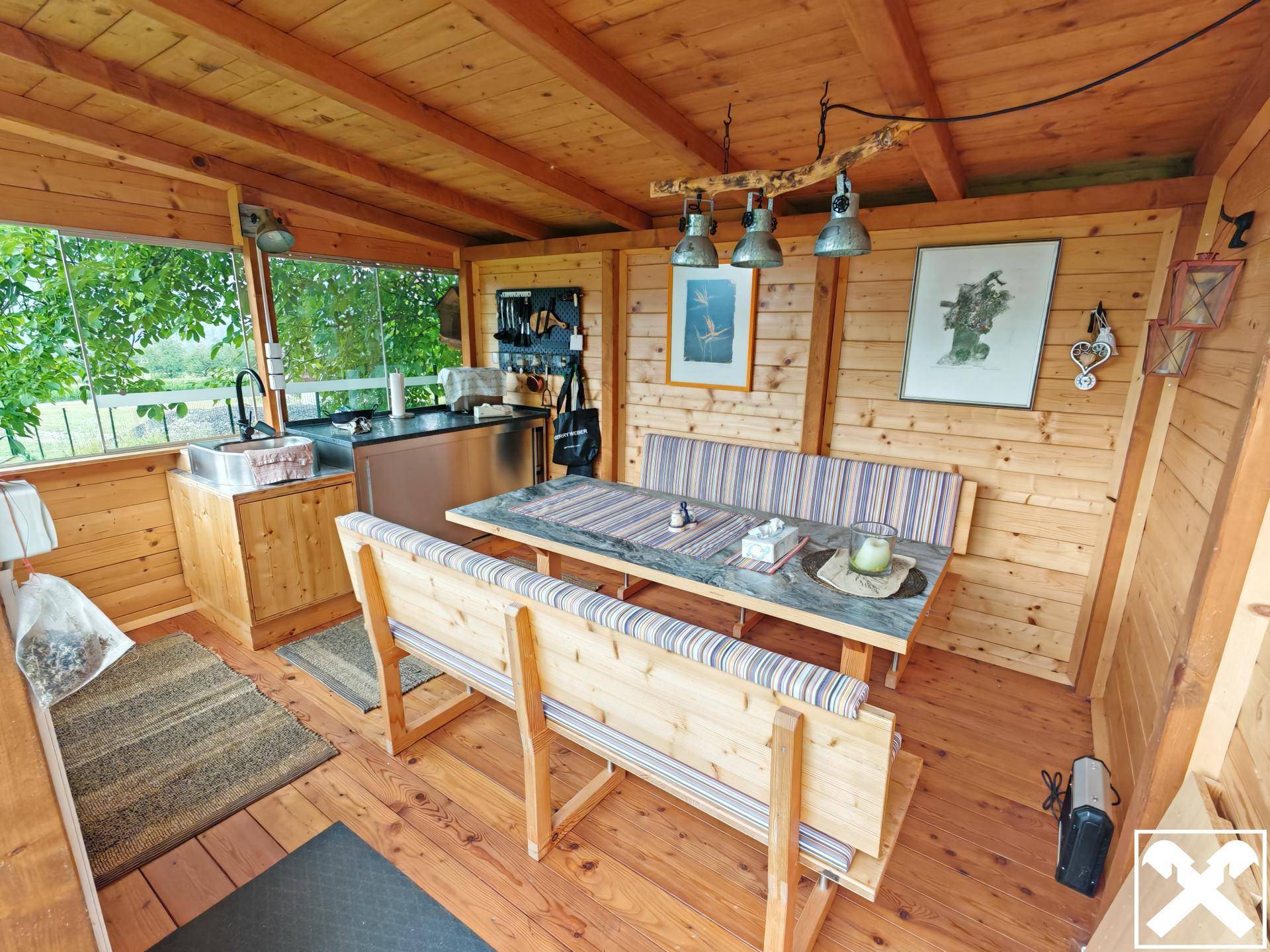 Gemütlicher Essbereich im Gartenhaus mit Holzbänken und kleiner Küchenzeile, ideal für gesellige Stunden.