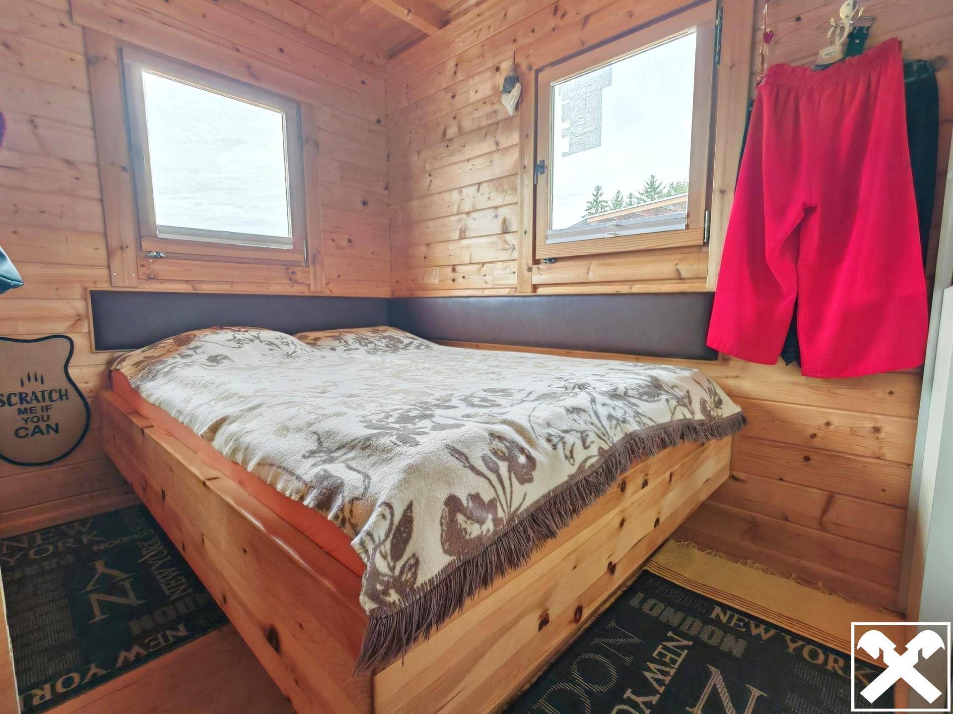 Rustikales Schlafzimmer mit Holzbett und Holzwänden, das eine warme und gemütliche Atmosphäre schafft.