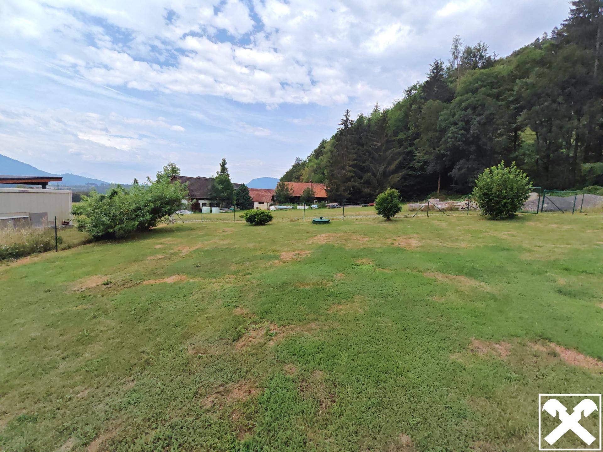 Weitläufige Rasenfläche mit Sträuchern und Bäumen, umgeben von einer ruhigen Landschaft mit Fernblick.