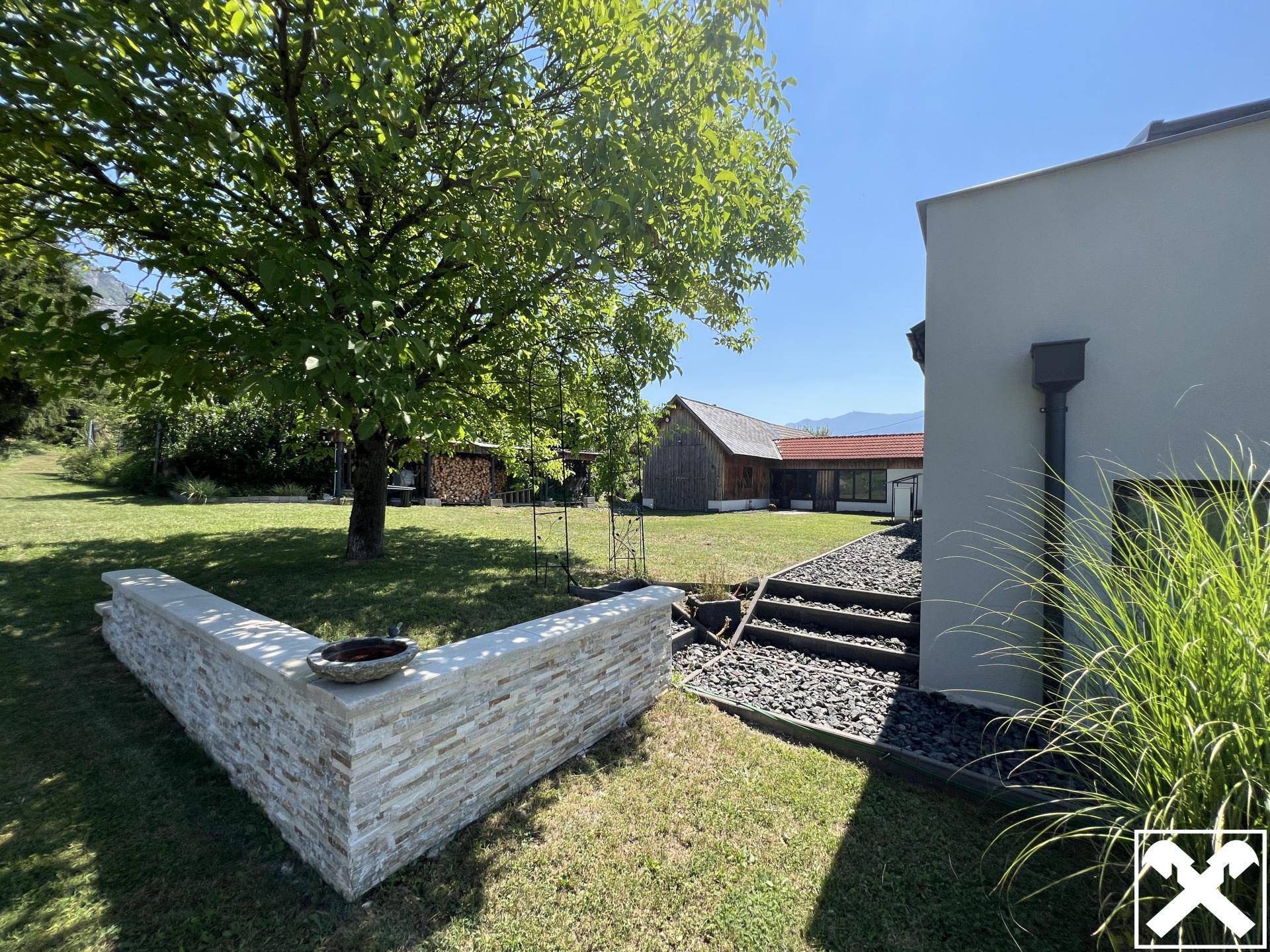 Moderne Hausfassade mit Steinelementen, gepflegtem Rasen und Blick auf traditionelle Gebäude.
