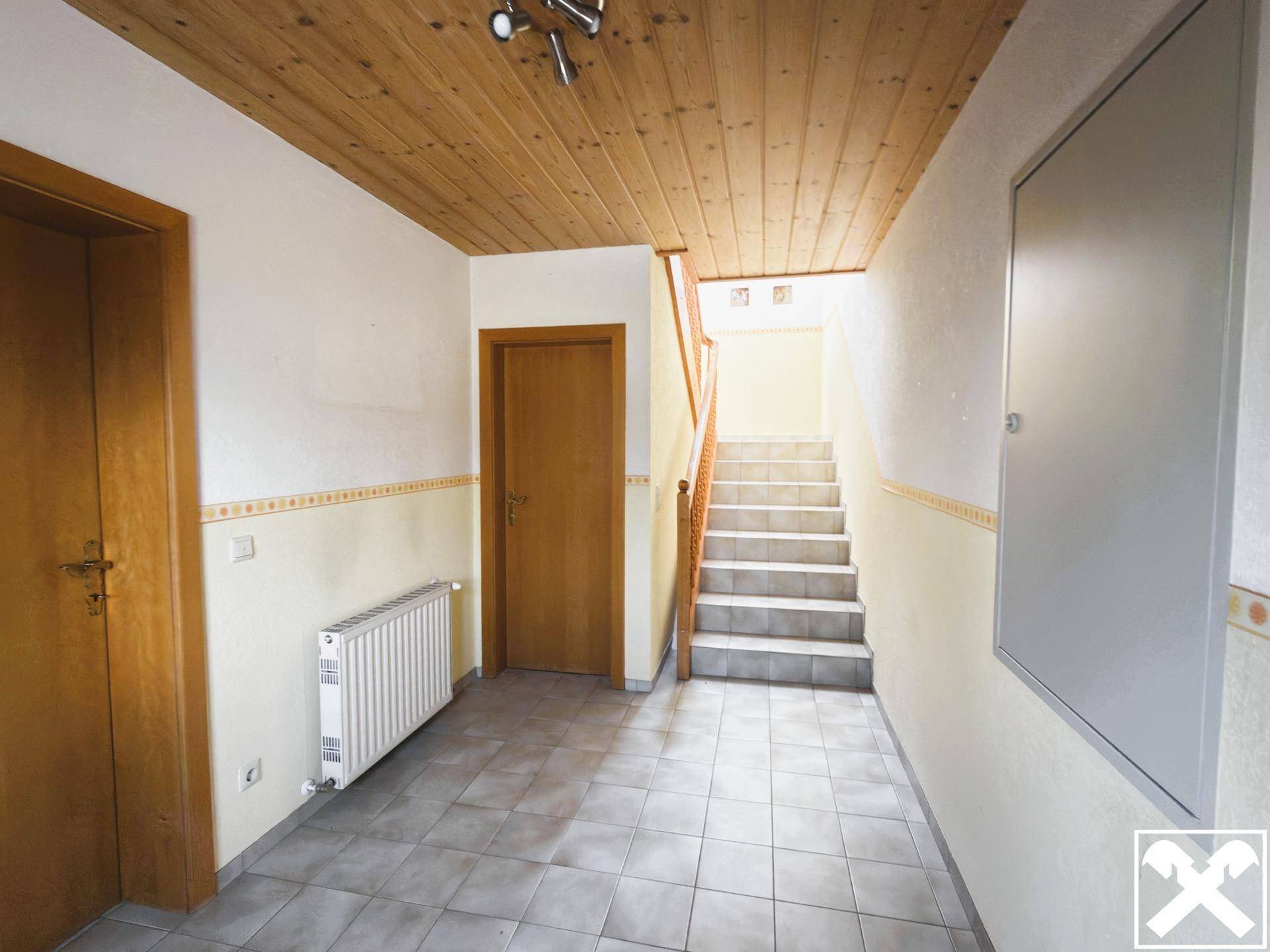 Heller Flur mit Holzdecke, Fliesenboden und Treppenaufgang in die obere Etage.
