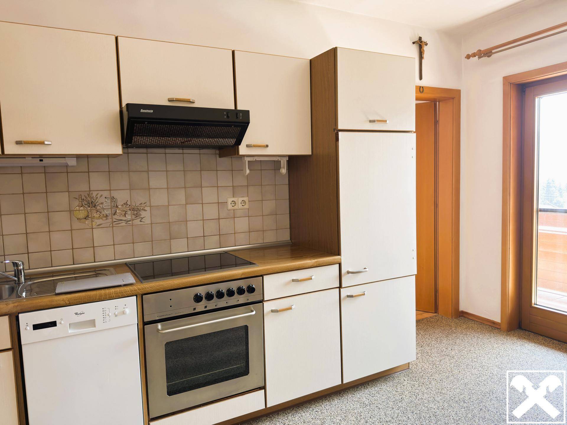 Funktionale Küche mit Einbaugeräten, Fliesenrückwand und Zugang zu einem Balkon.