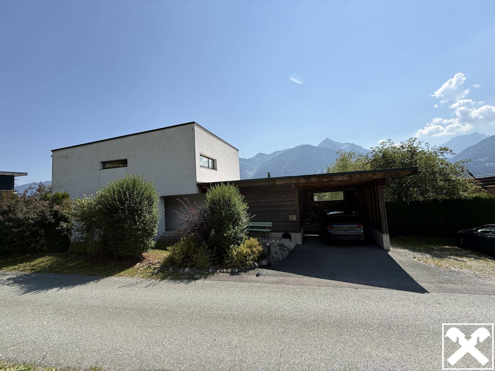 Modernes Haus mit Carport und Blick auf die umliegende Berglandschaft unter blauem Himmel.