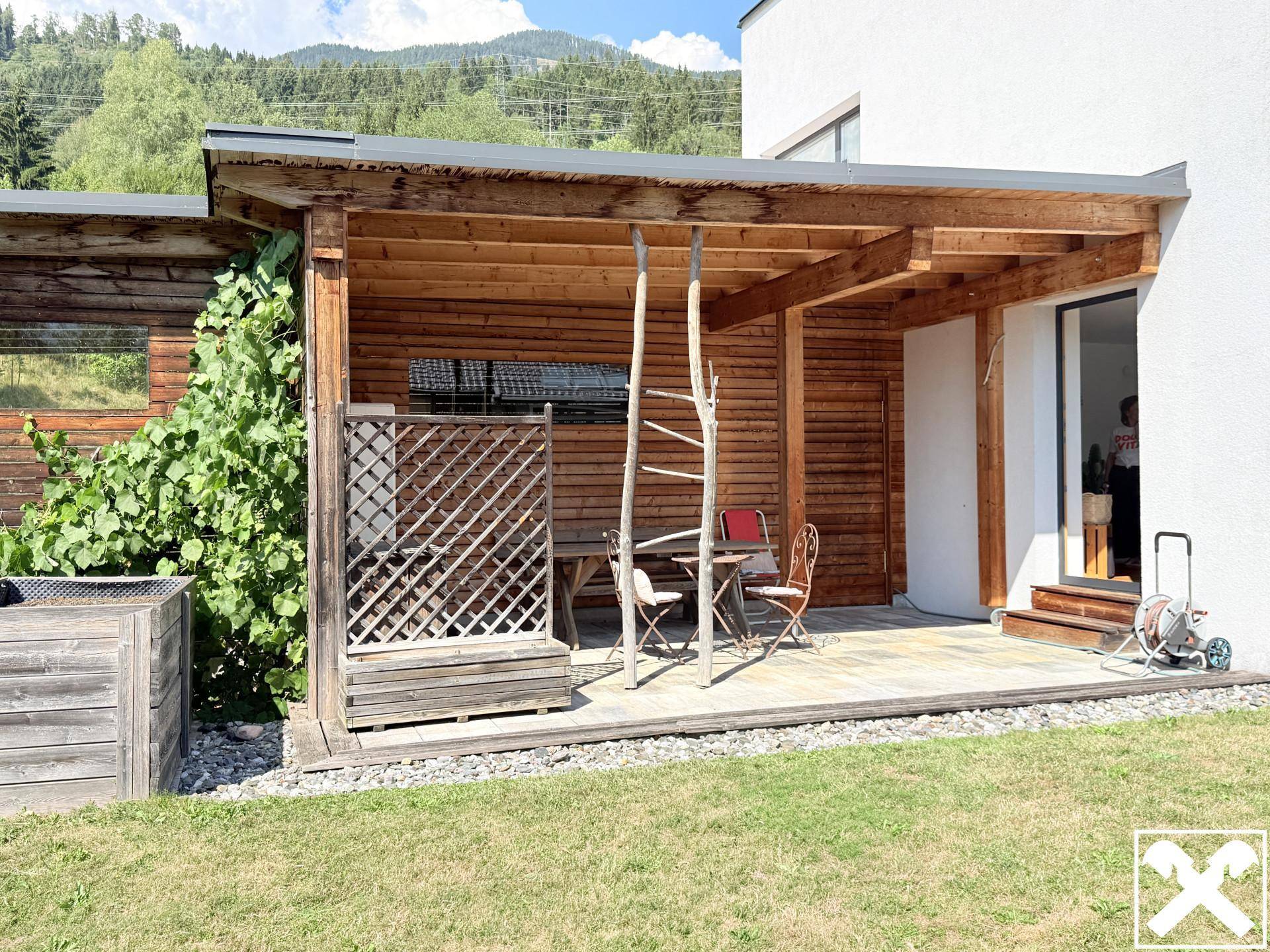 Überdachte Holzterrasse mit Sitzgelegenheiten und Blick auf den grünen Gartenbereich.