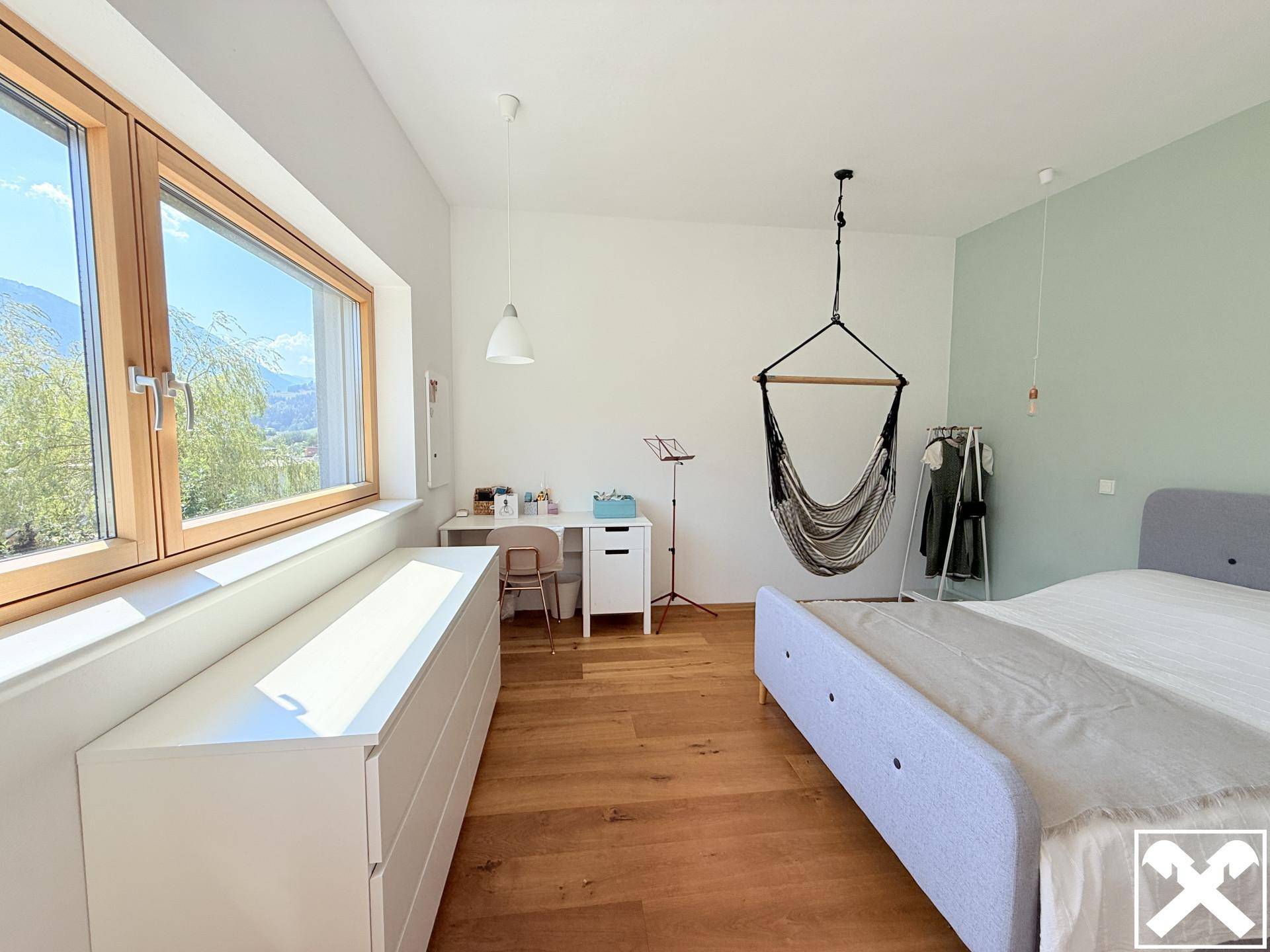 Helles Schlafzimmer mit Holzboden, großem Fenster und Schreibtischbereich.