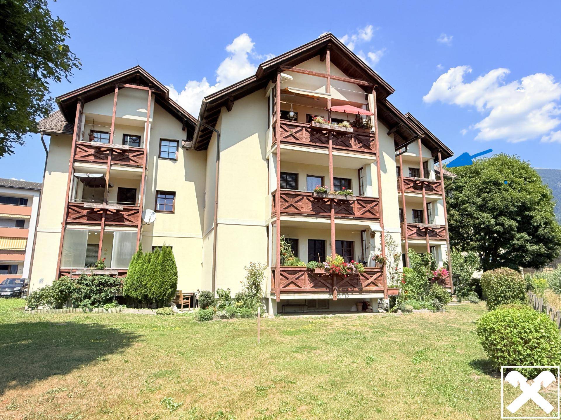 Mehrfamilienhaus mit traditionellen Holzbalkonen und gepflegter Grünfläche im Vordergrund.