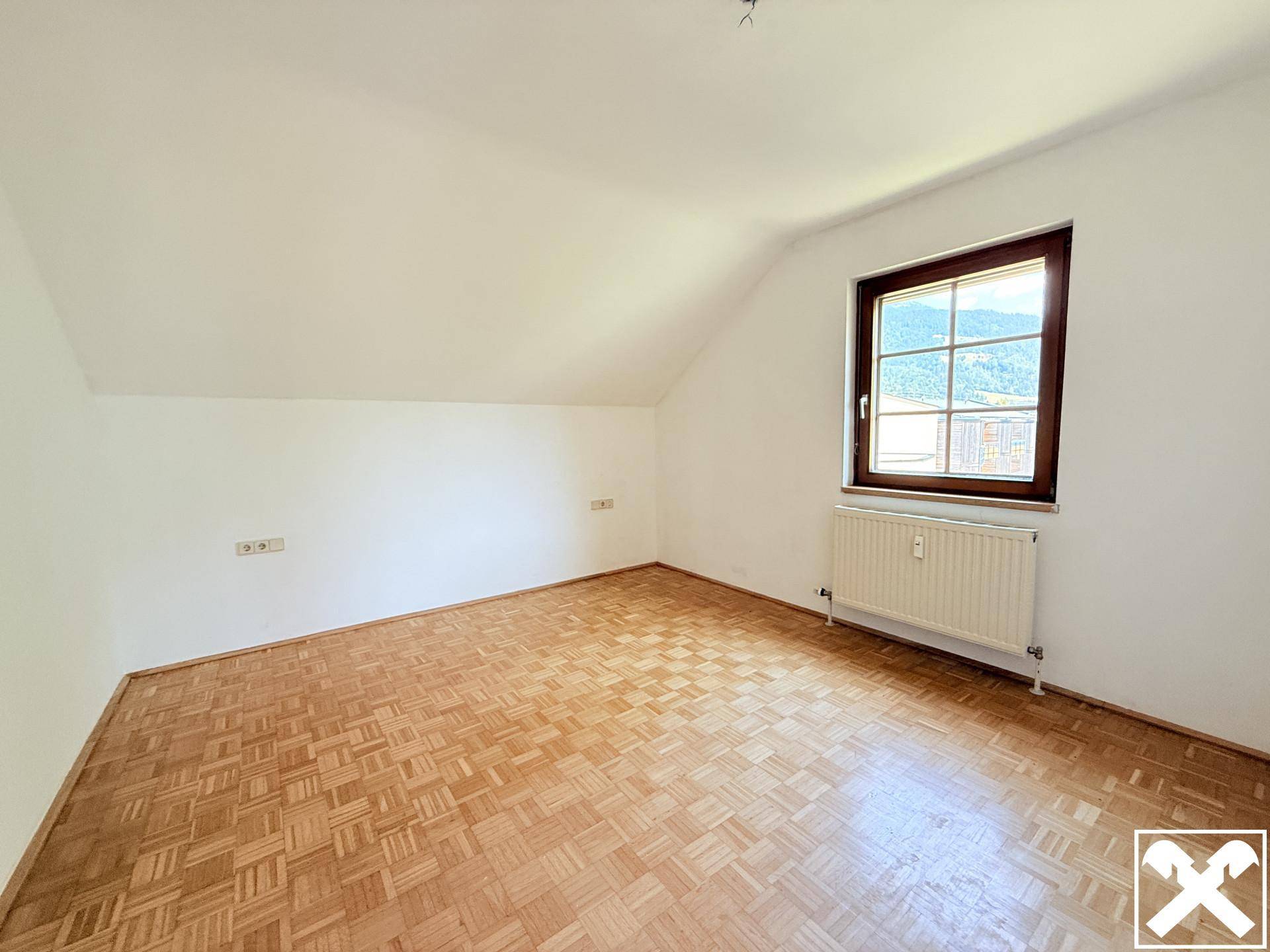Schlafzimmer mit hellem Parkettboden, Dachschräge und einem Fenster mit Bergblick.