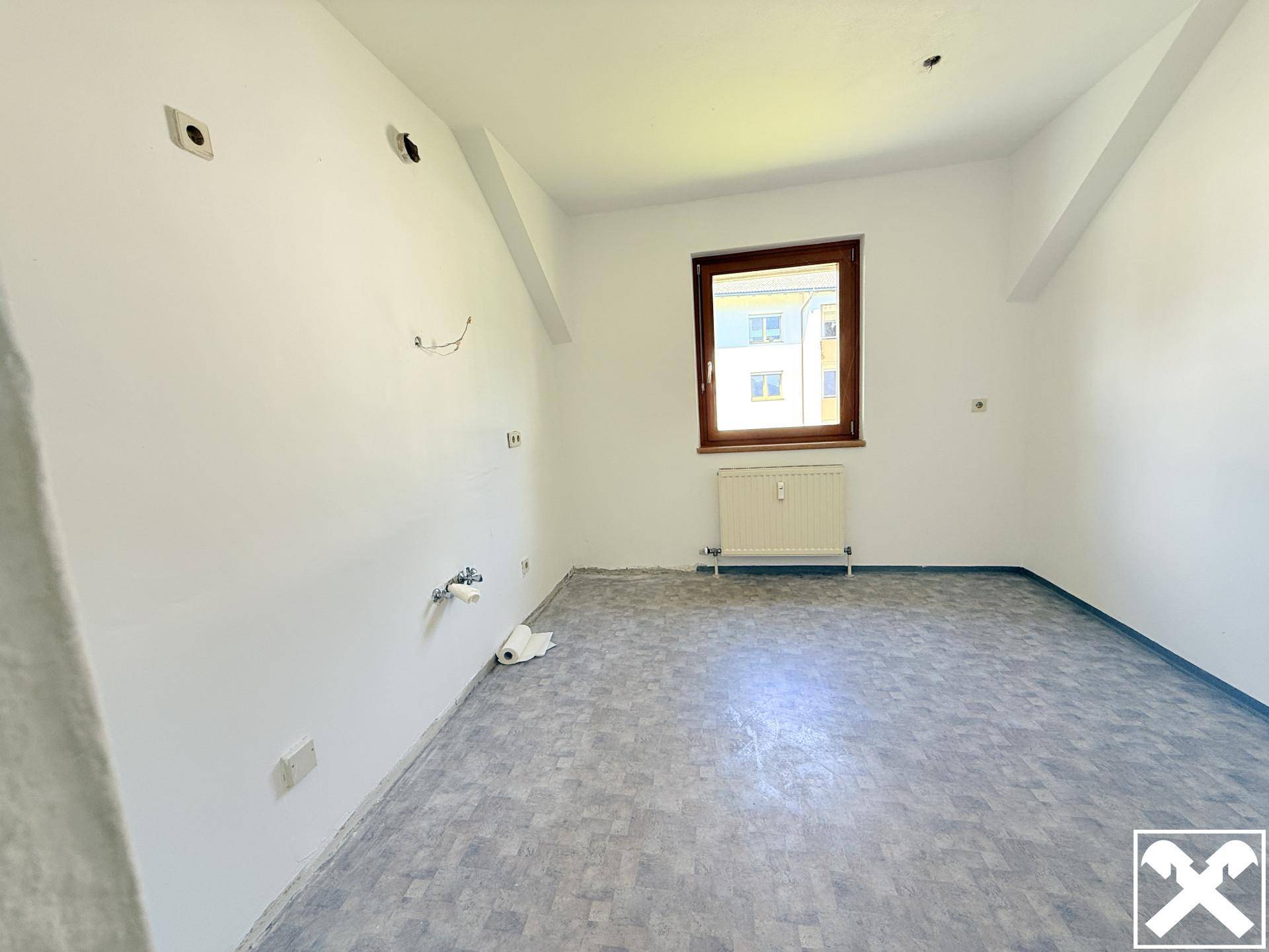 Unfertige Küche mit Vinylboden und Anschlüssen für Spüle und Geräte, bereit zum Ausbau.