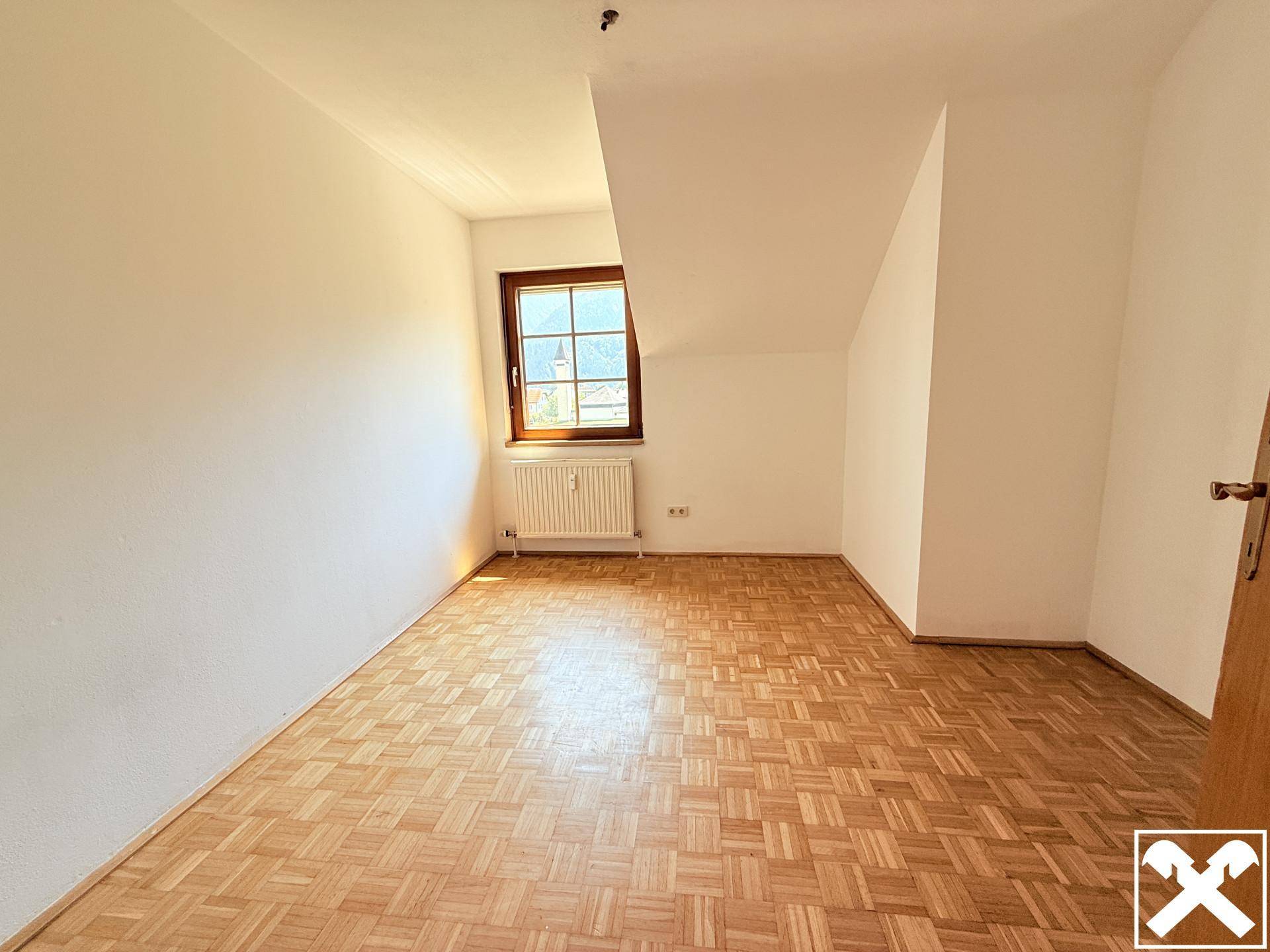 Helles Schlafzimmer mit Parkettboden, Dachschräge und einem Fenster mit Blick nach draußen.