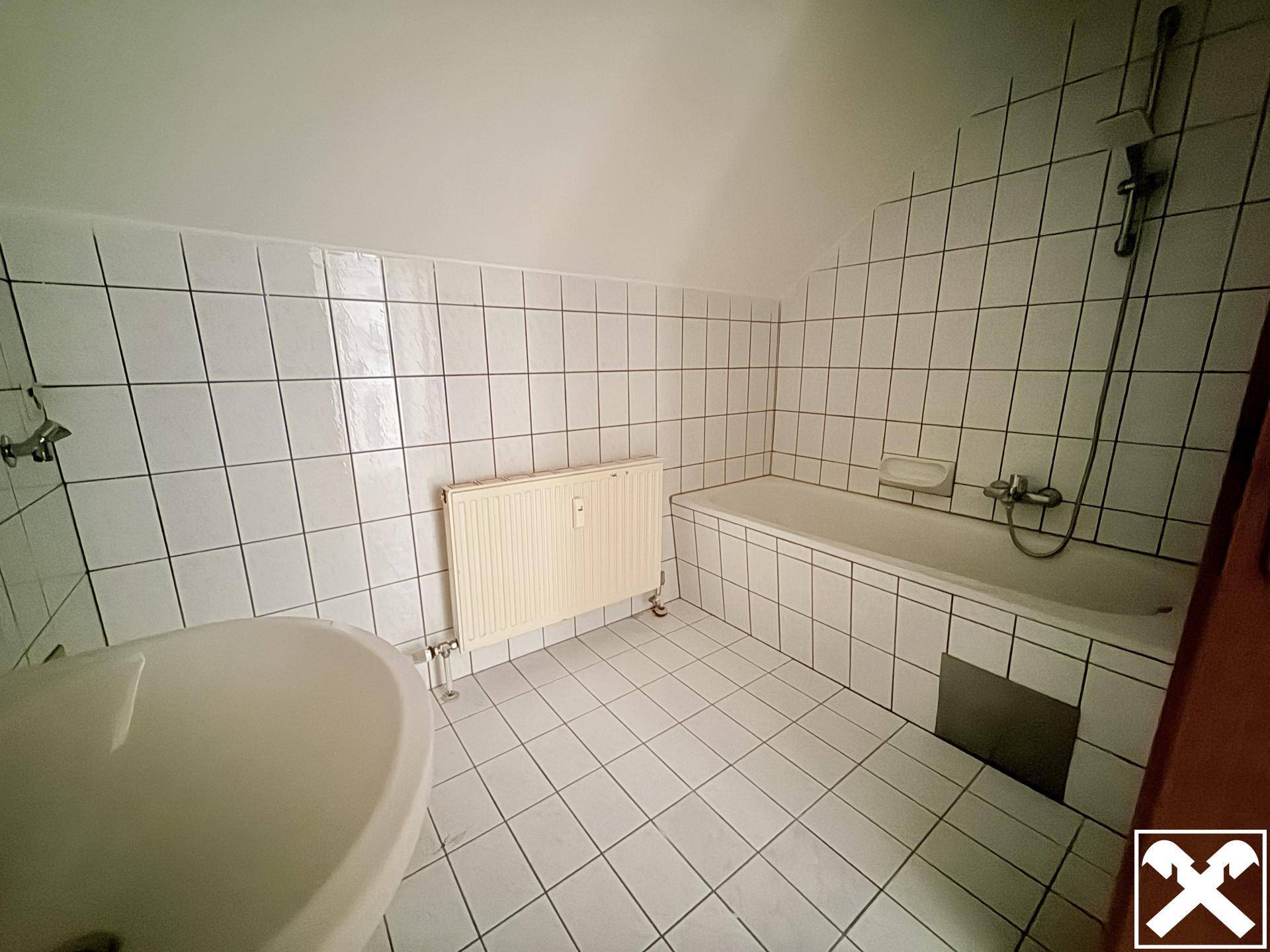Badezimmer mit weißen Fliesen, Badewanne und Waschbecken, unter einer Dachschräge gelegen.