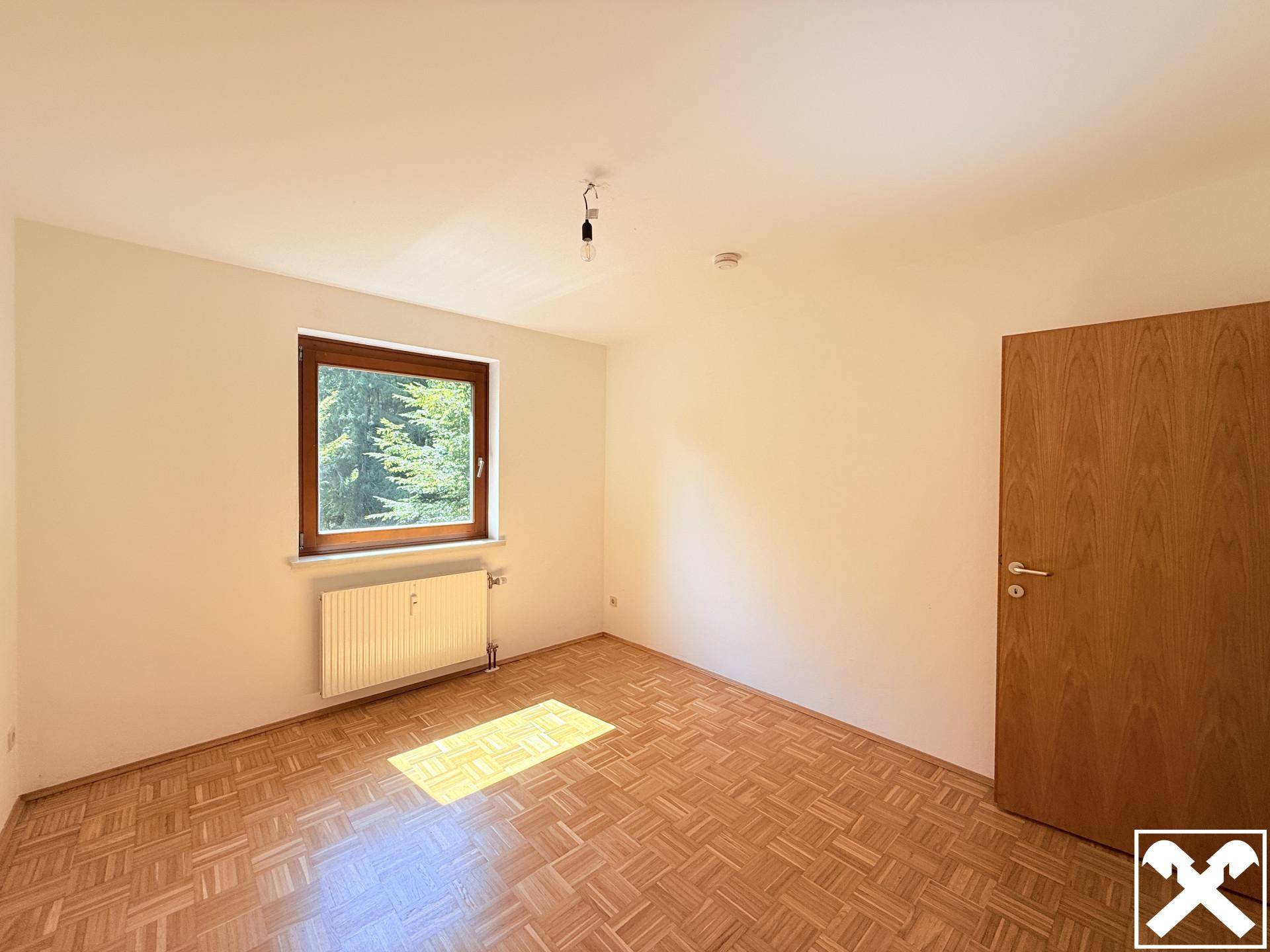 Geräumiges Schlafzimmer mit hellem Parkettboden und einer Holztür, gut beleuchtet.