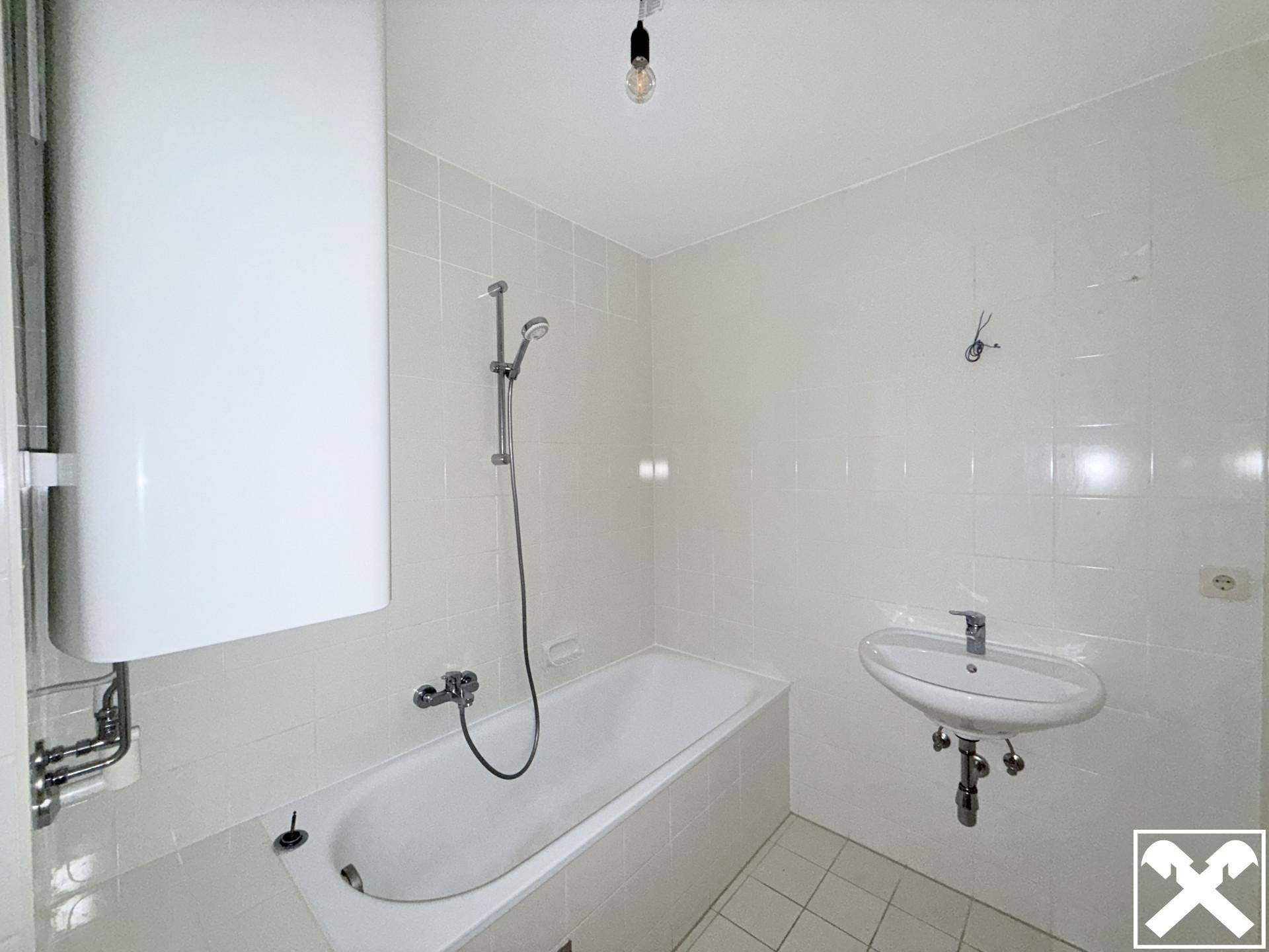 Funktionales Badezimmer mit weißen Fliesen, Badewanne mit Duschfunktion und Waschbecken.