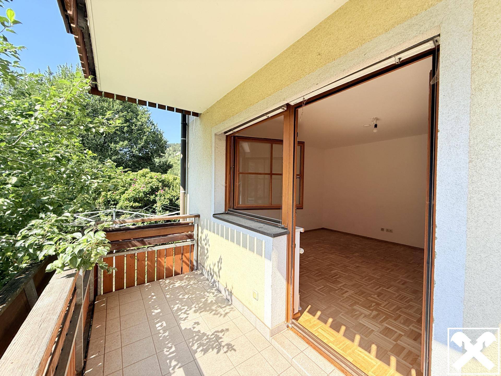 Gefliester Balkon mit Zugang zu einem hellen Innenraum, umgeben von üppigem Grün.