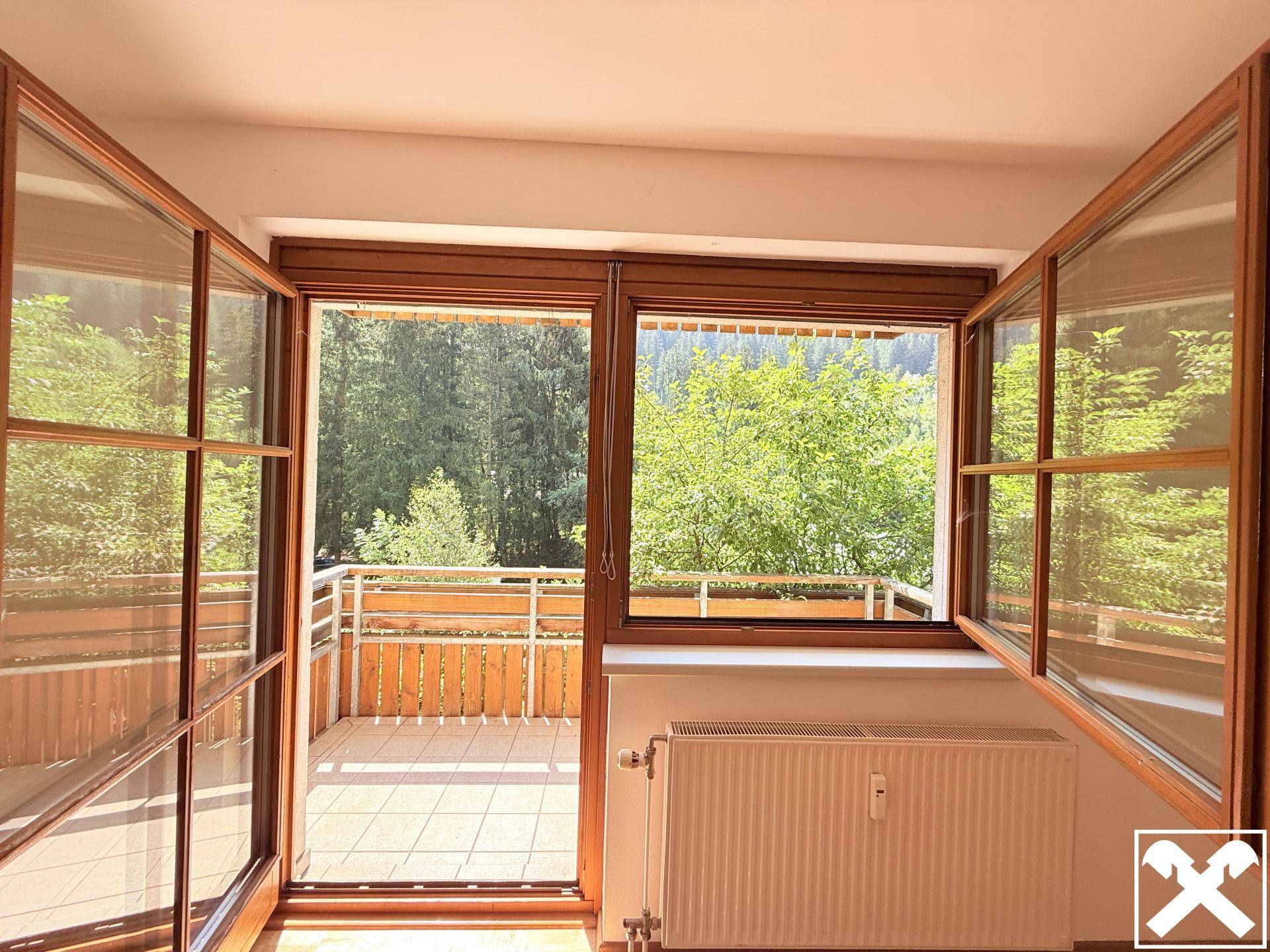 Heller Innenraum mit Holztüren und Blick auf einen gefliesten Balkon sowie die grüne Umgebung.