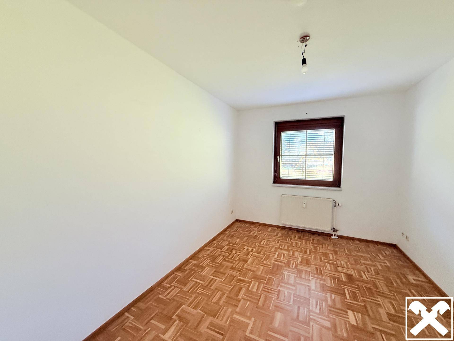Leeres Schlafzimmer mit Parkettboden und einem Fenster mit Jalousien, bereit zur individuellen Gestaltung.