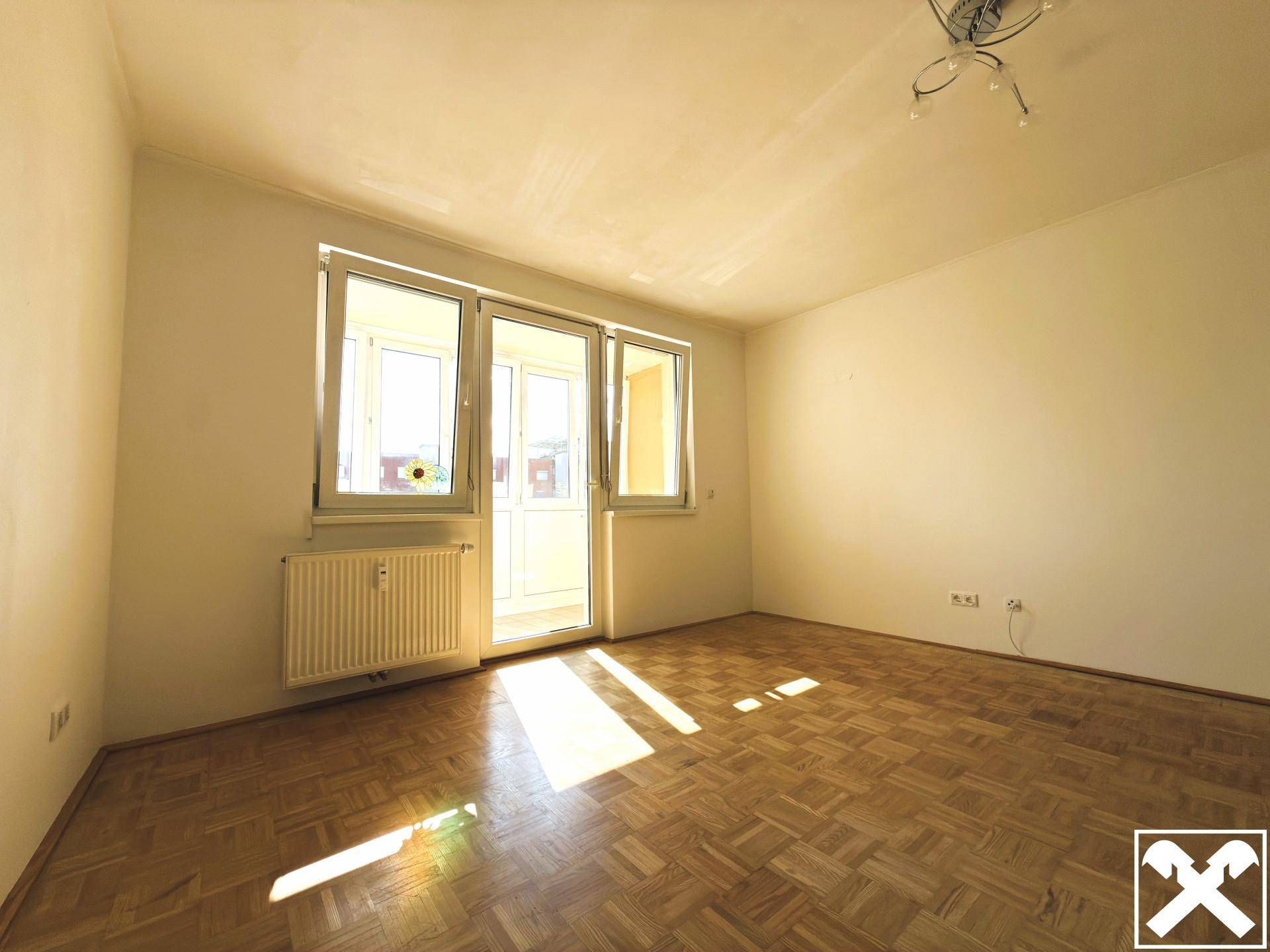Sonniger Raum mit Parkettboden und Zugang zu einem Balkon oder einer Loggia.