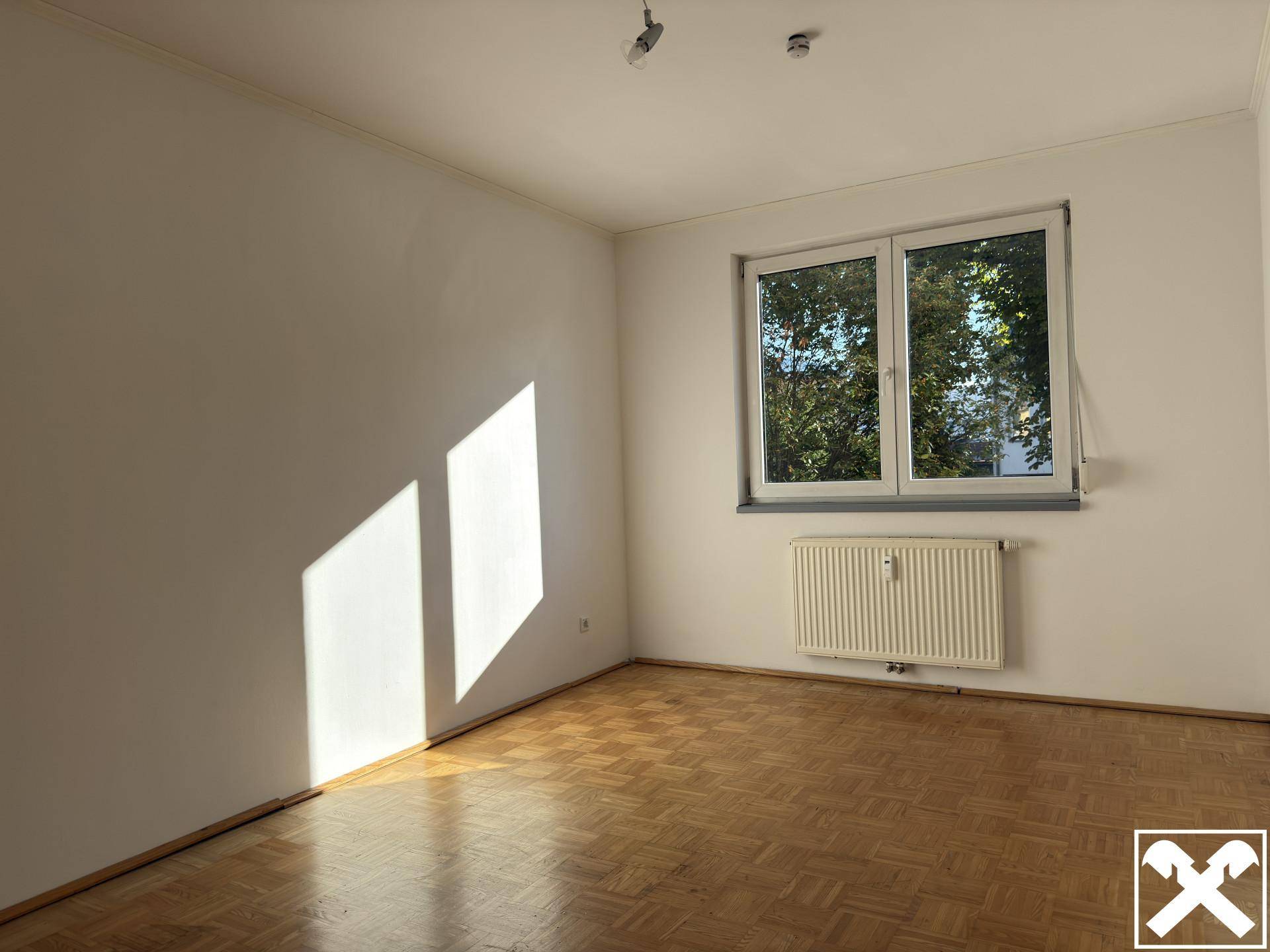 Helles Schlafzimmer mit Parkettboden und großem Fenster mit Blick ins Grüne.