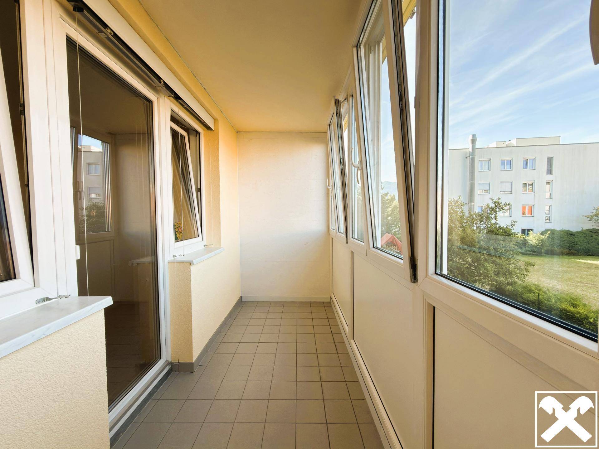 Verglaste Loggia mit Fliesenboden und Blick auf die umliegenden Gebäude und Grünflächen.