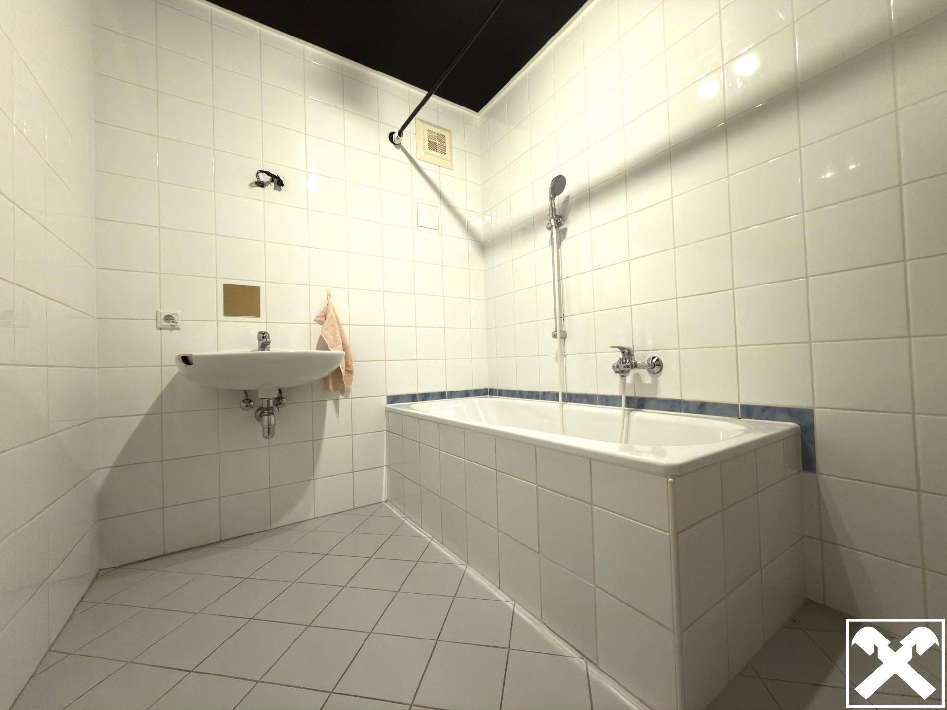 Gefliestes Badezimmer mit Badewanne und Waschbecken in schlichtem Design.