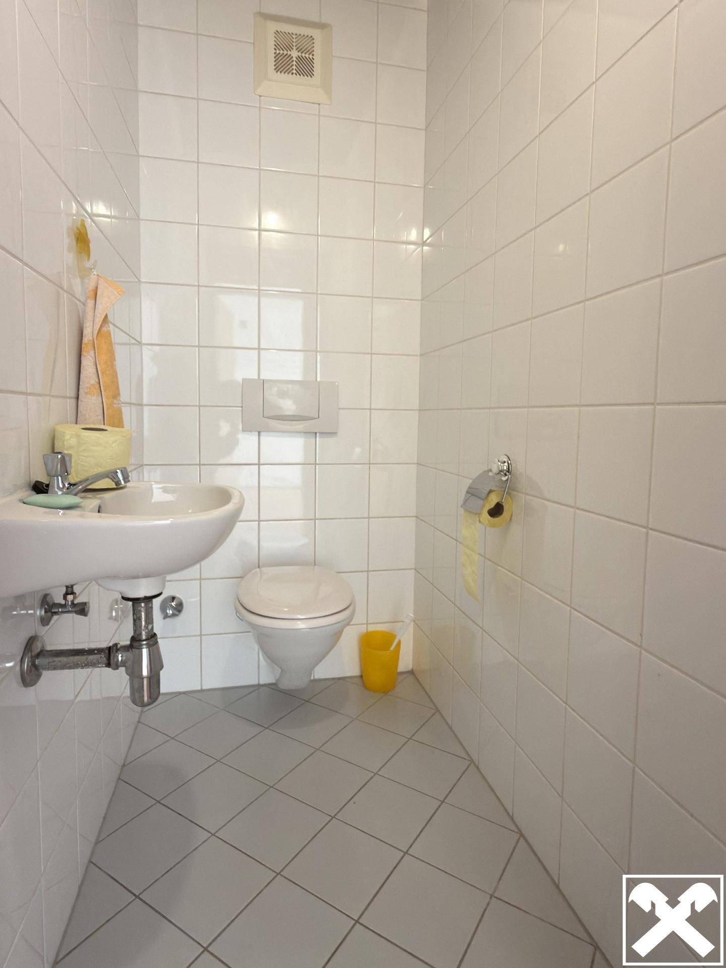 Separates WC mit Wand-WC, kleinem Waschbecken und weißen Fliesen.