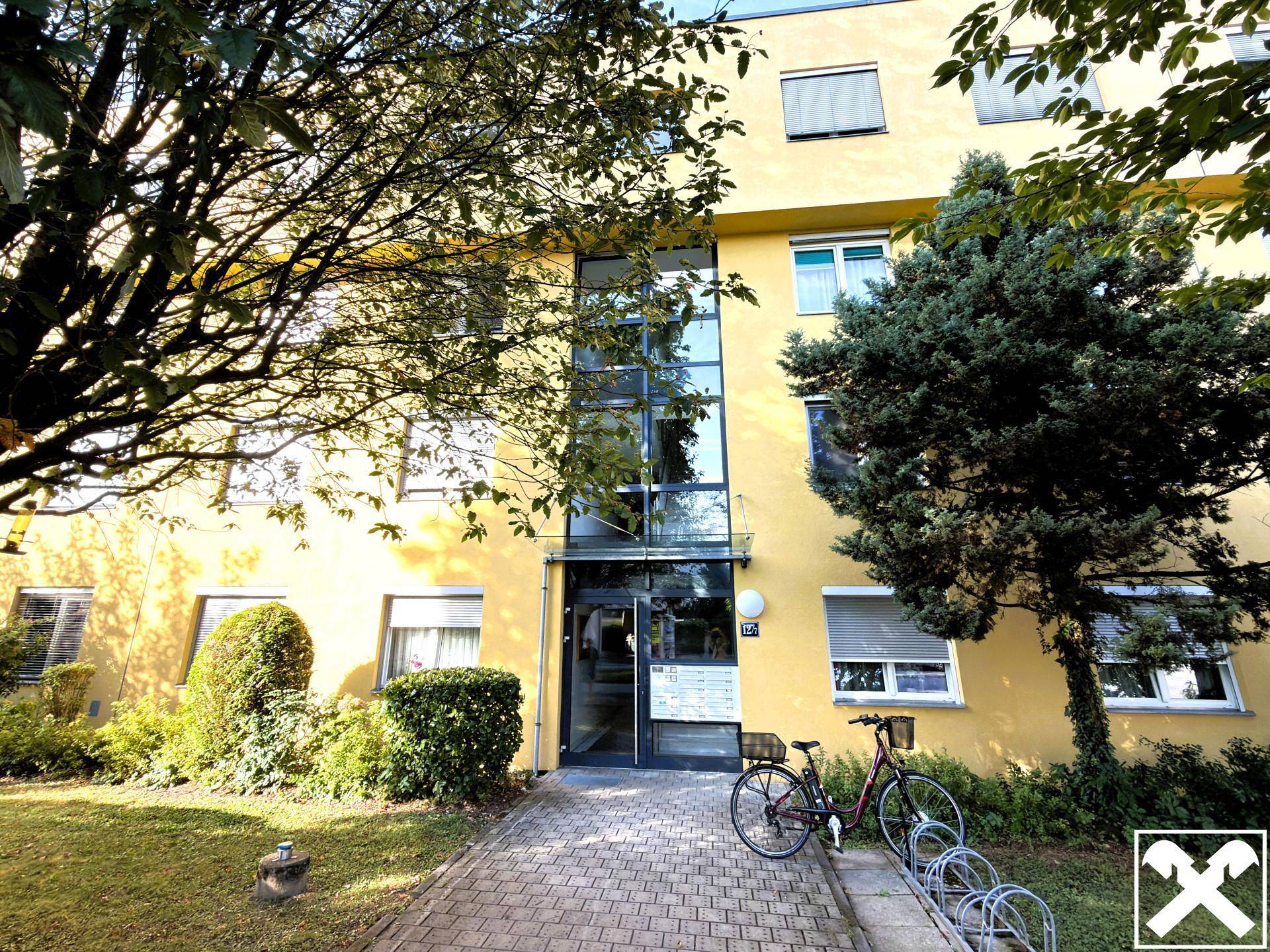 Eingangsbereich eines gelben Wohnhauses mit Glasfassade und Fahrradständern.