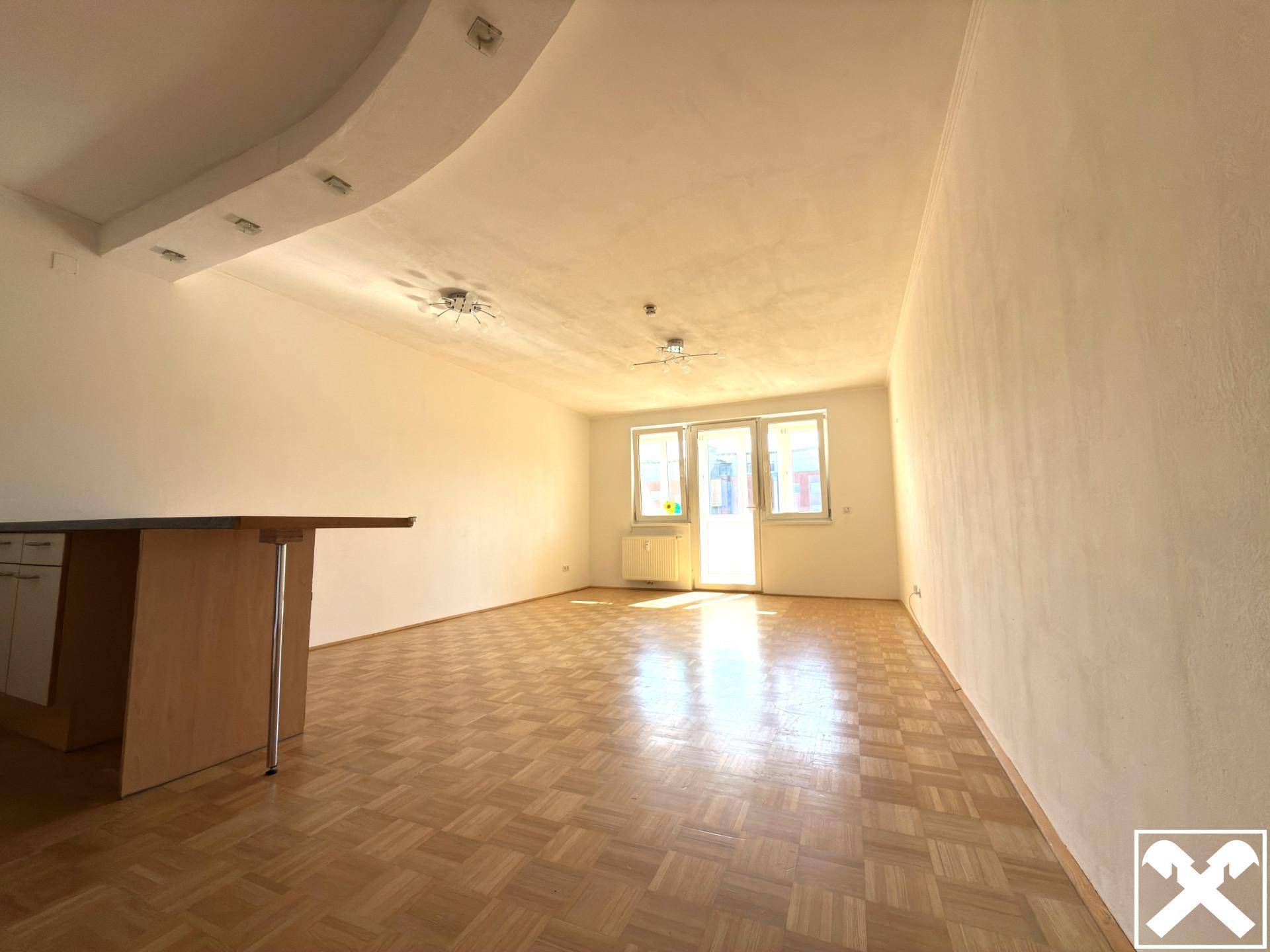 Heller Wohnbereich mit Parkettboden und Zugang zu einem Balkon oder einer Loggia.
