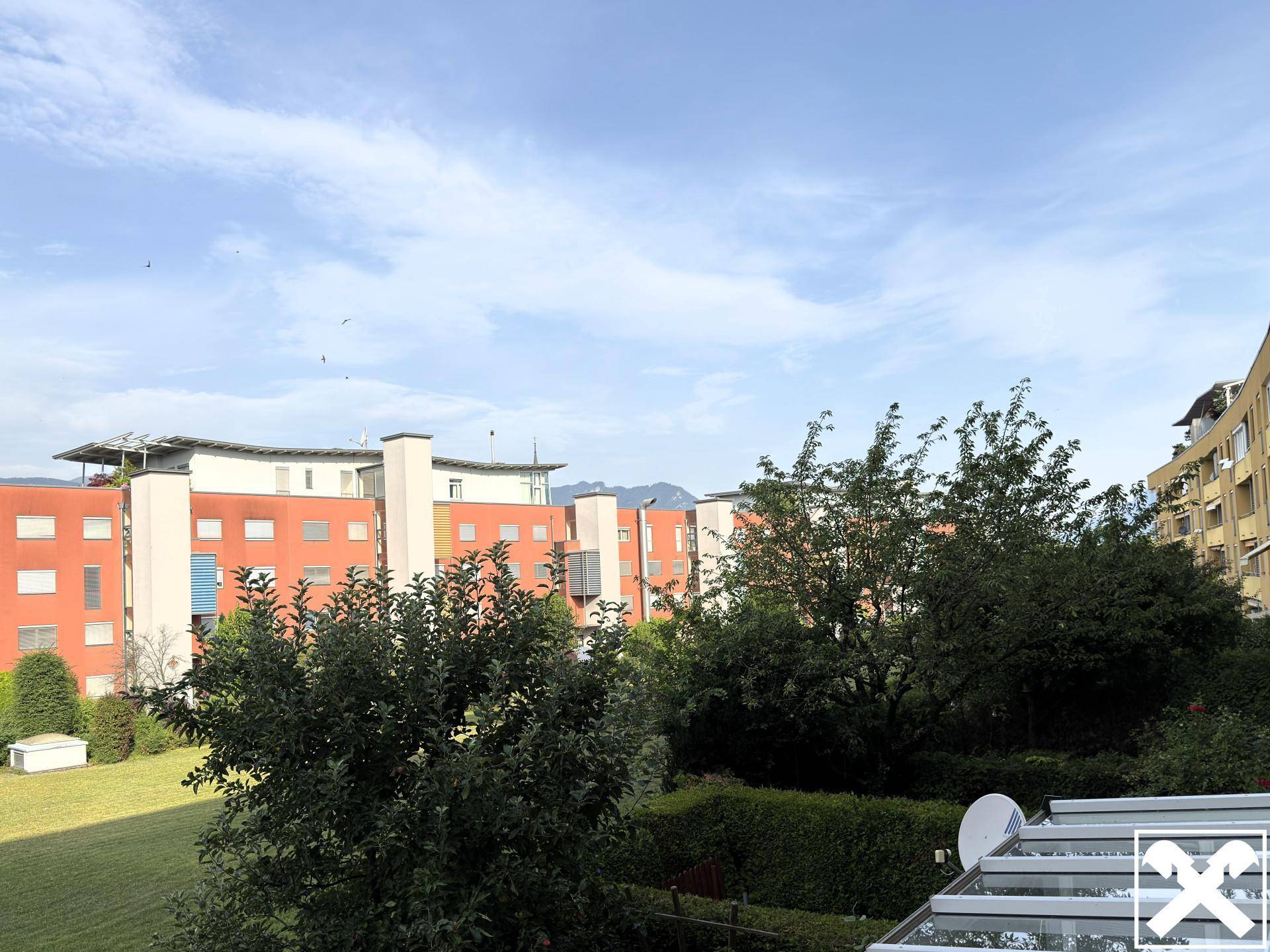 Panoramablick auf die umliegende Wohnbebauung und grüne Hügel unter blauem Himmel.