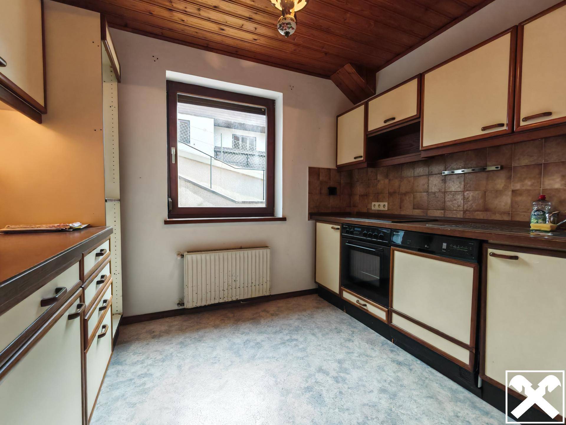 Ältere Küche mit Holzdecke, Fliesenboden und Einbauschränken, bereit zur Modernisierung.